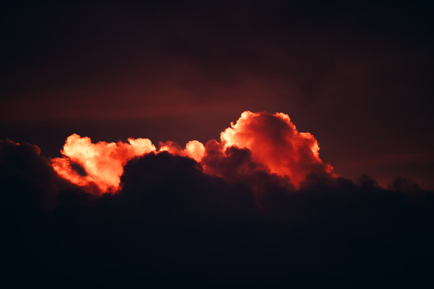 Dark sky with illuminated orange and red clouds glowing from sunset or sunrise.