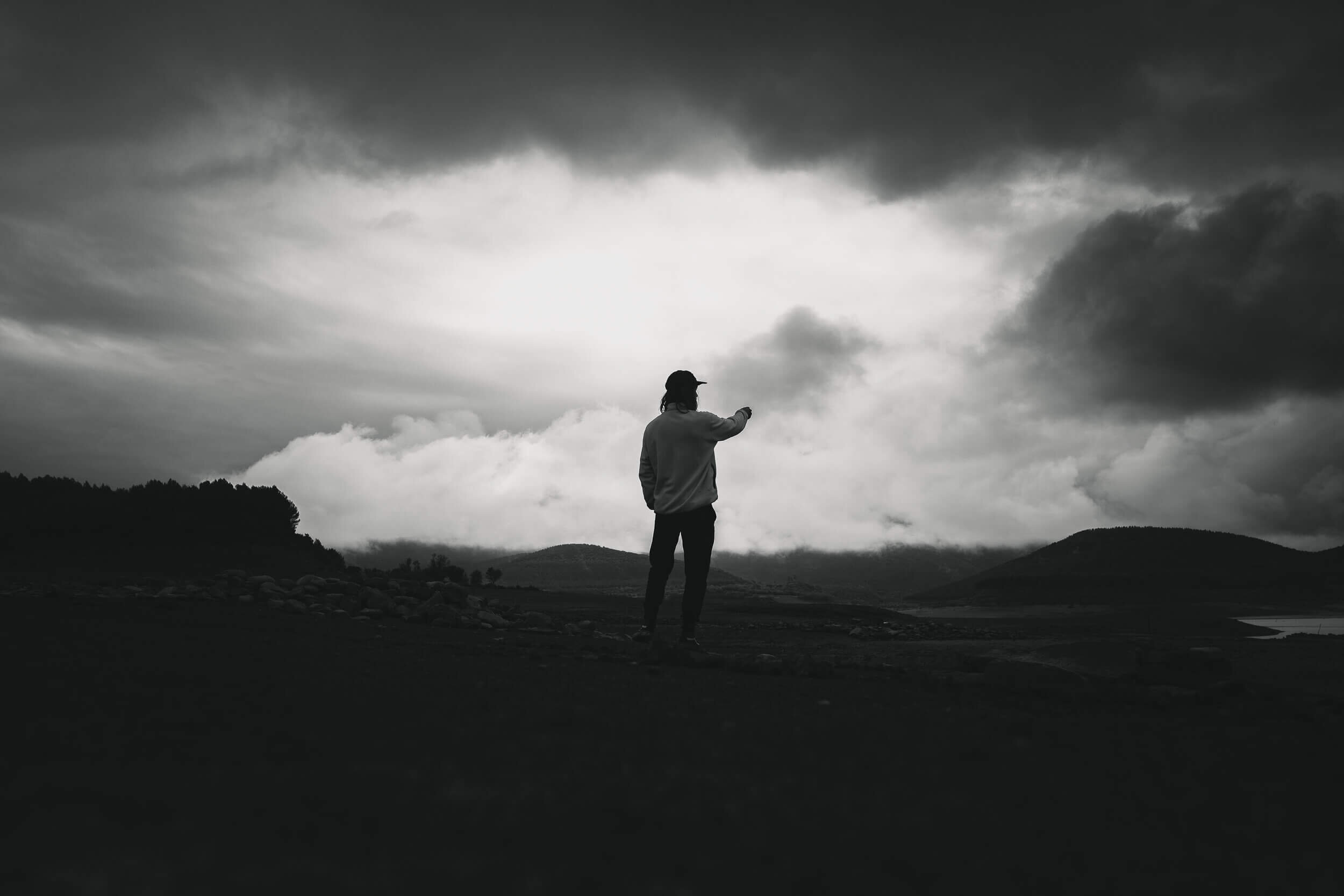 Une silhouette d'homme portant une casquette, debout dans un paysage nuageux et sombre, pointant vers le ciel.