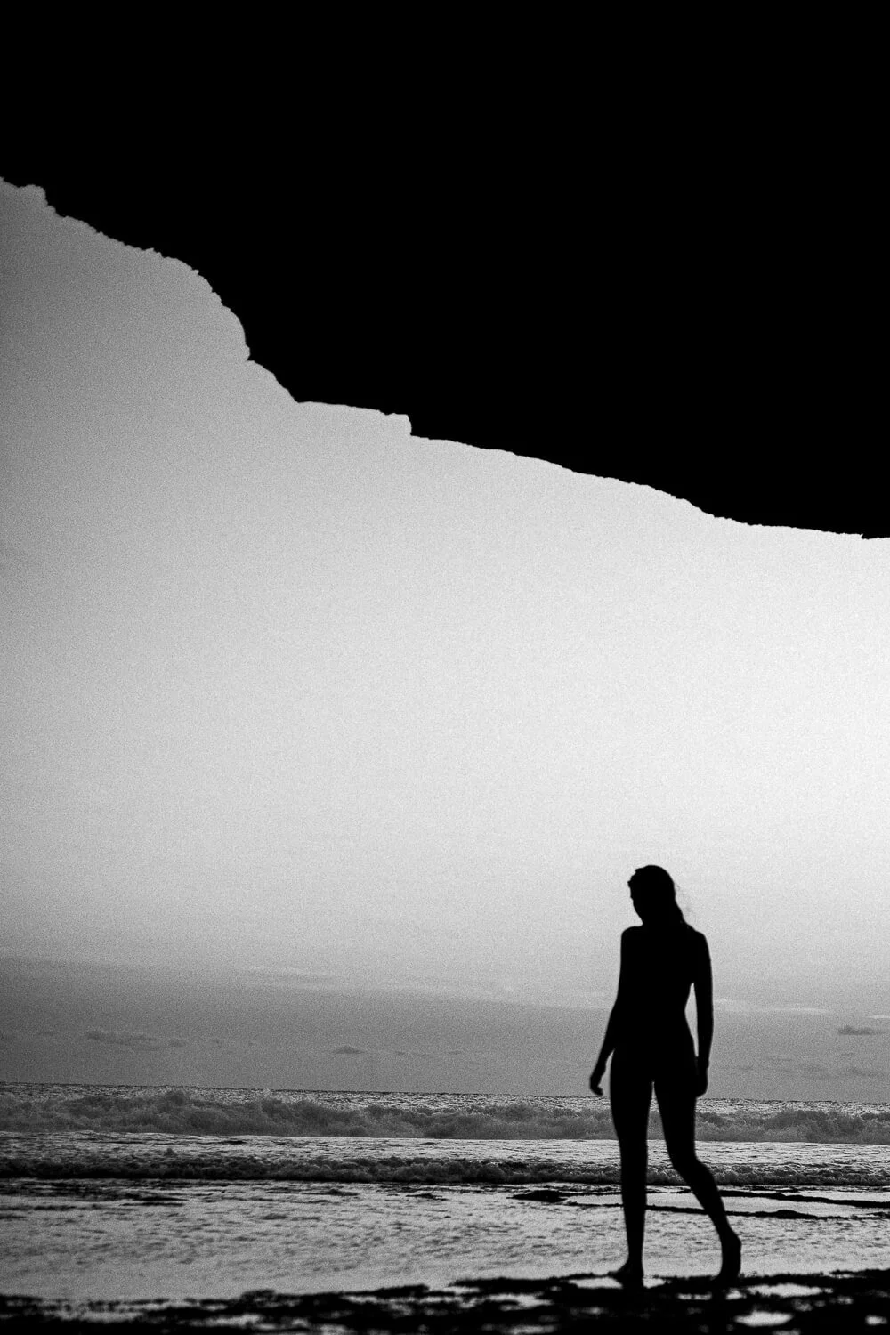 Silhouette of a woman walking on the beach at sunset with the ocean waves in the background.