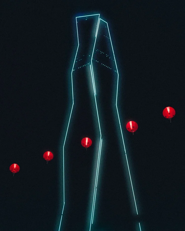 Une structure lumineuse en forme de pantalon suspendu dans le ciel, entourée de lanternes rouges flottantes.