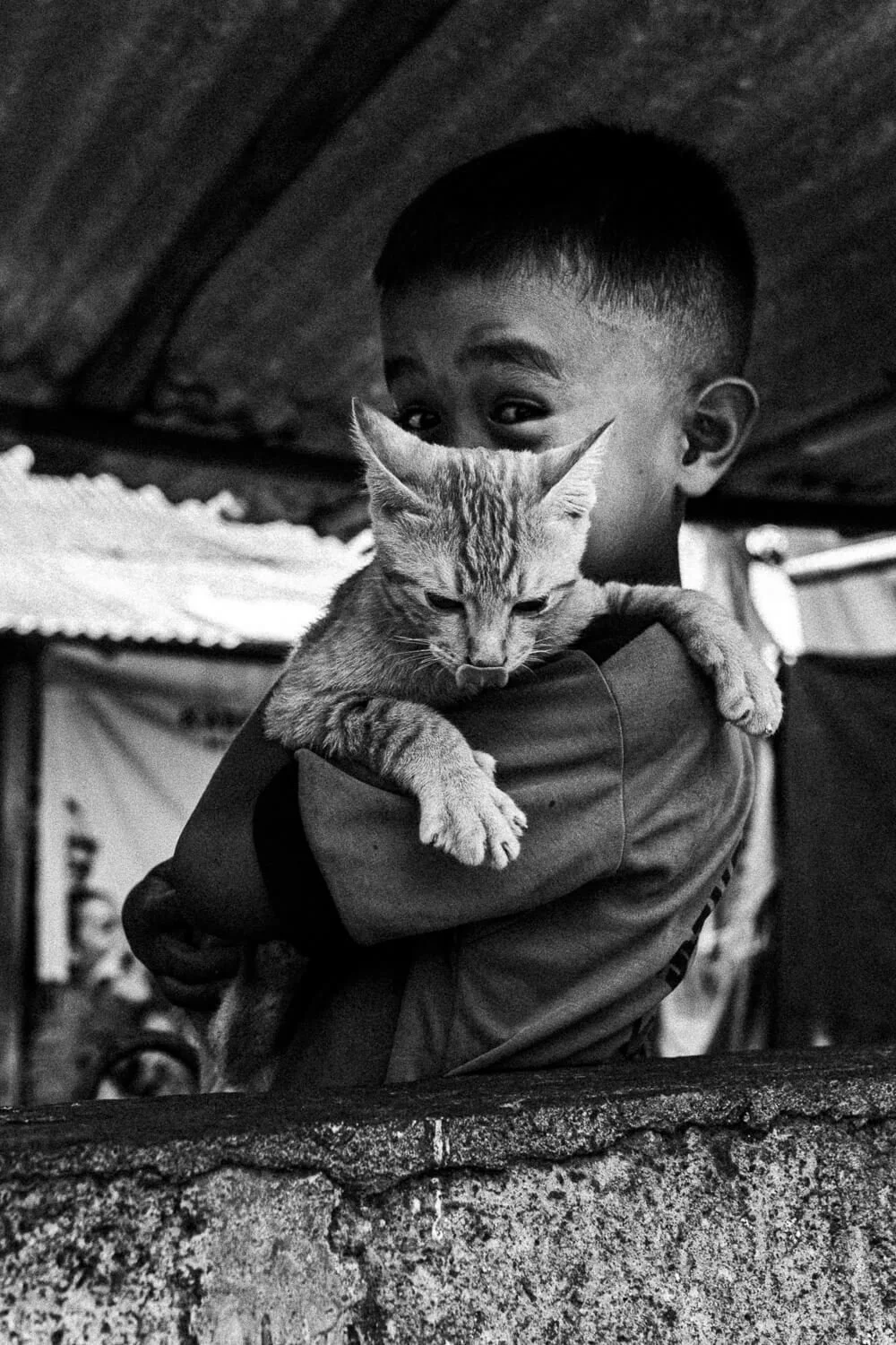 Un garçon noir tient un chat de race bengal dans ses bras, dans un environnement intérieur en noir et blanc.