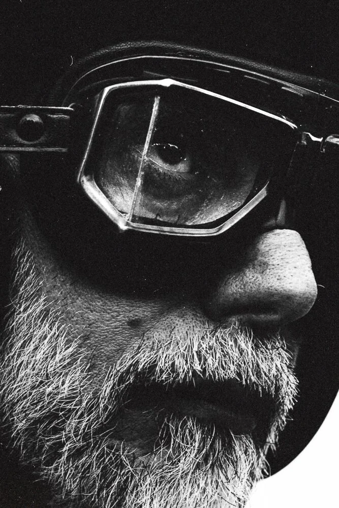 Close-up black-and-white photo of an older man with a white beard wearing goggles.