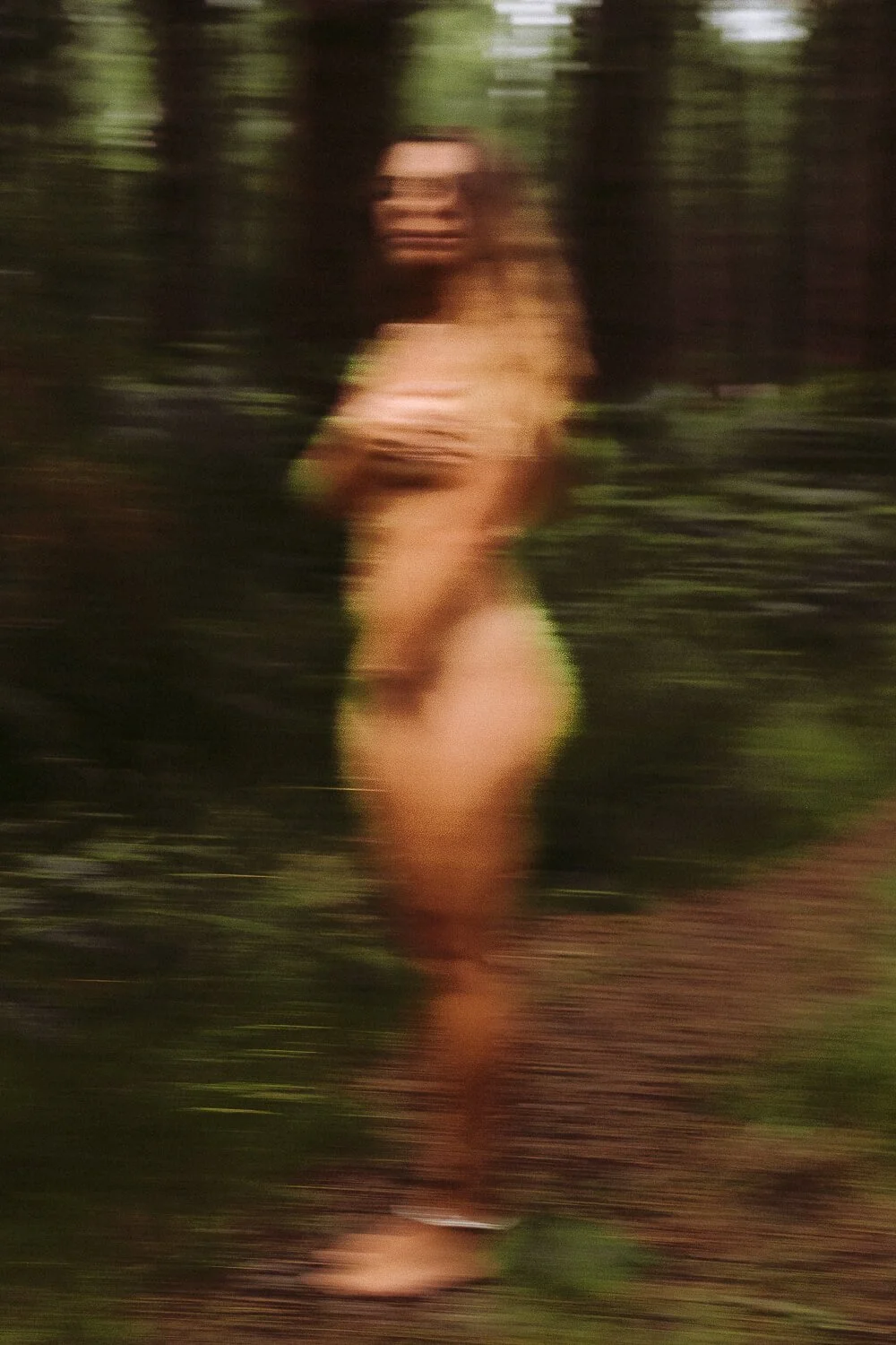 Blurred image of a person with long hair standing outdoors in a natural setting.