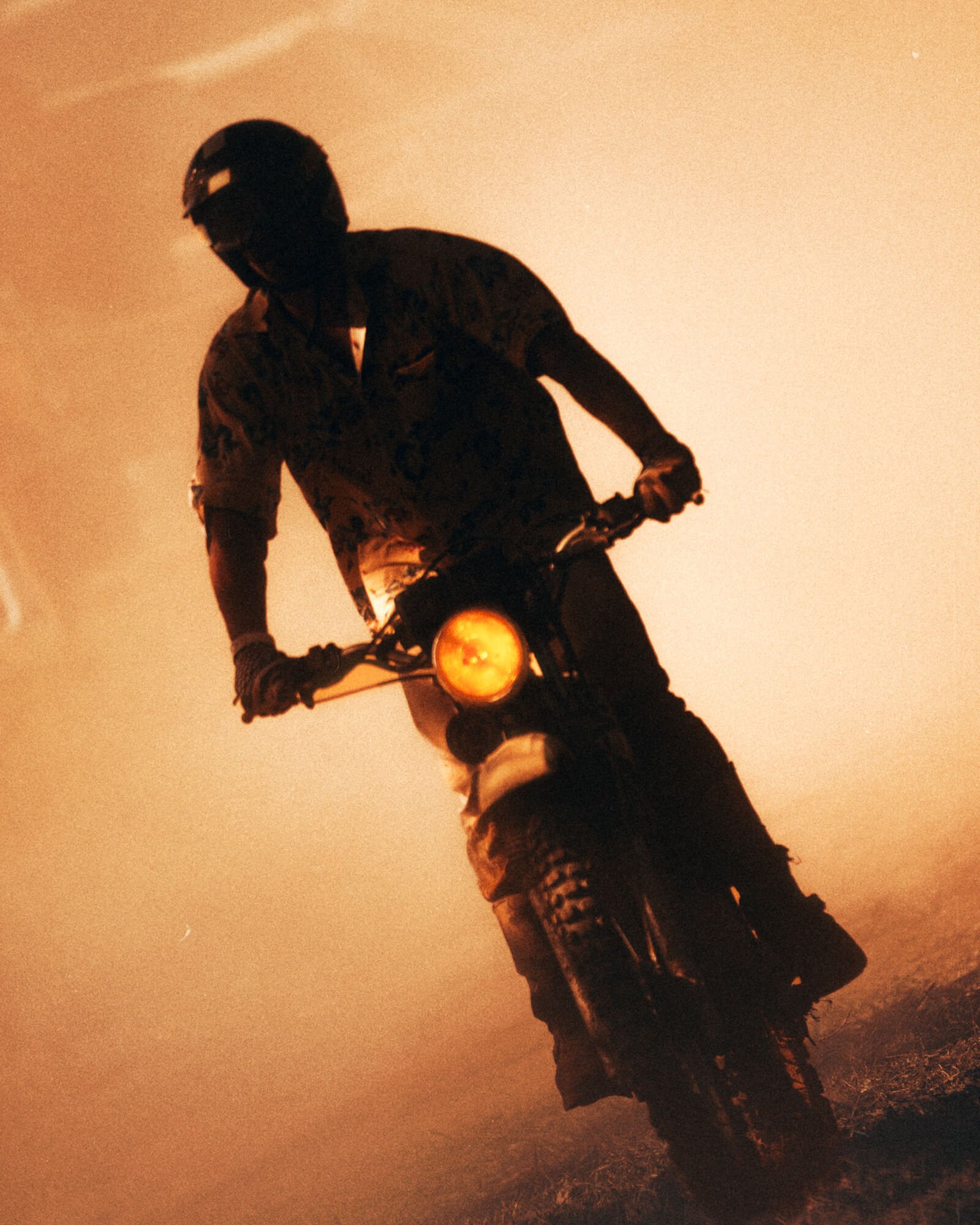 A person riding a dirt bike on a trail at sunset with a glowing orange sky.
