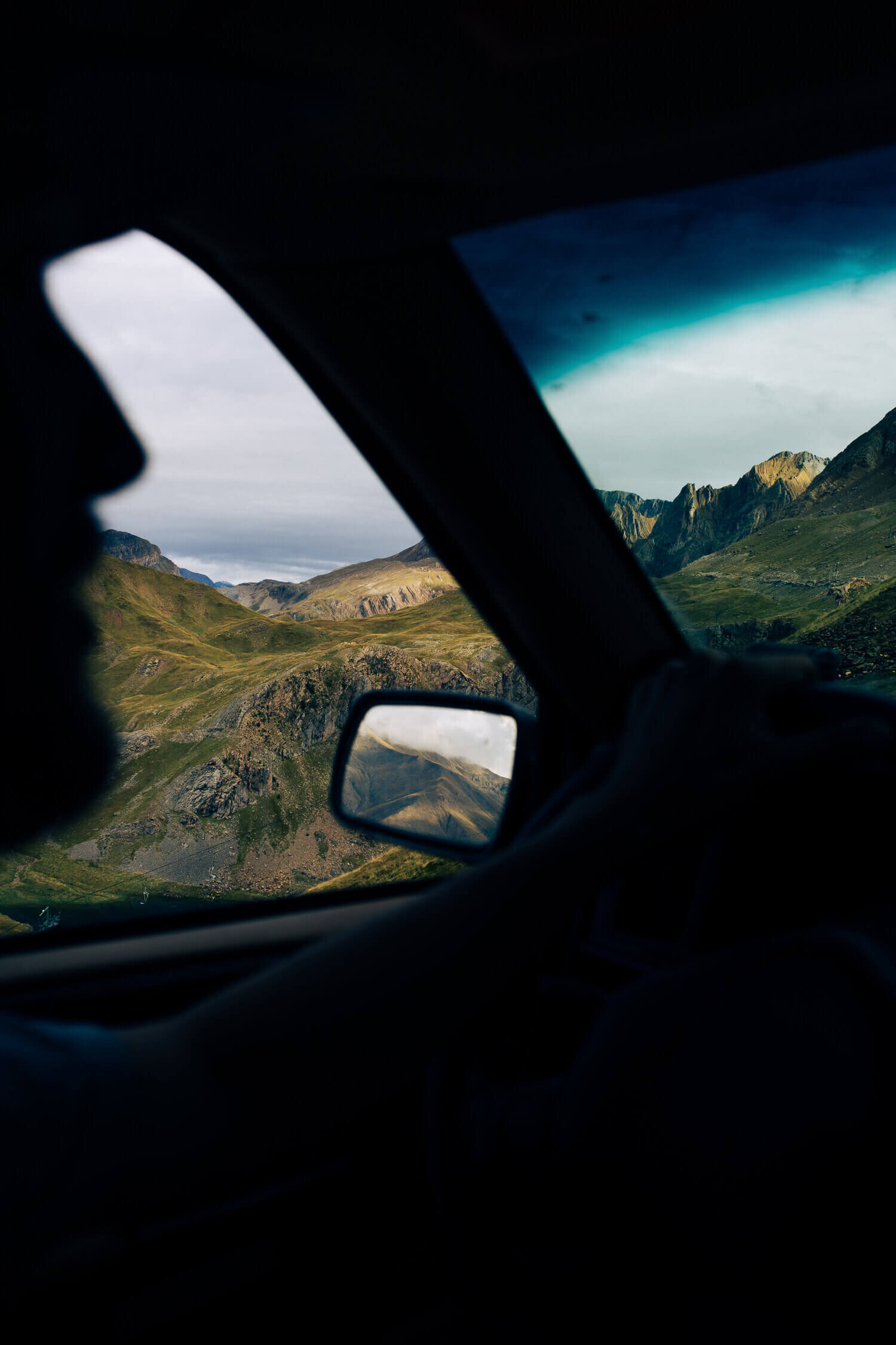 Vue d'un paysage montagneux par la fenêtre d'une voiture avec une personne en silhouette.