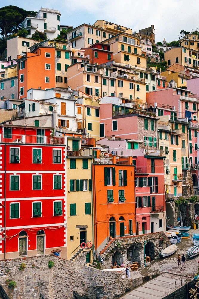 Colorful hillside buildings in a Mediterranean coastal town with boats docked below.