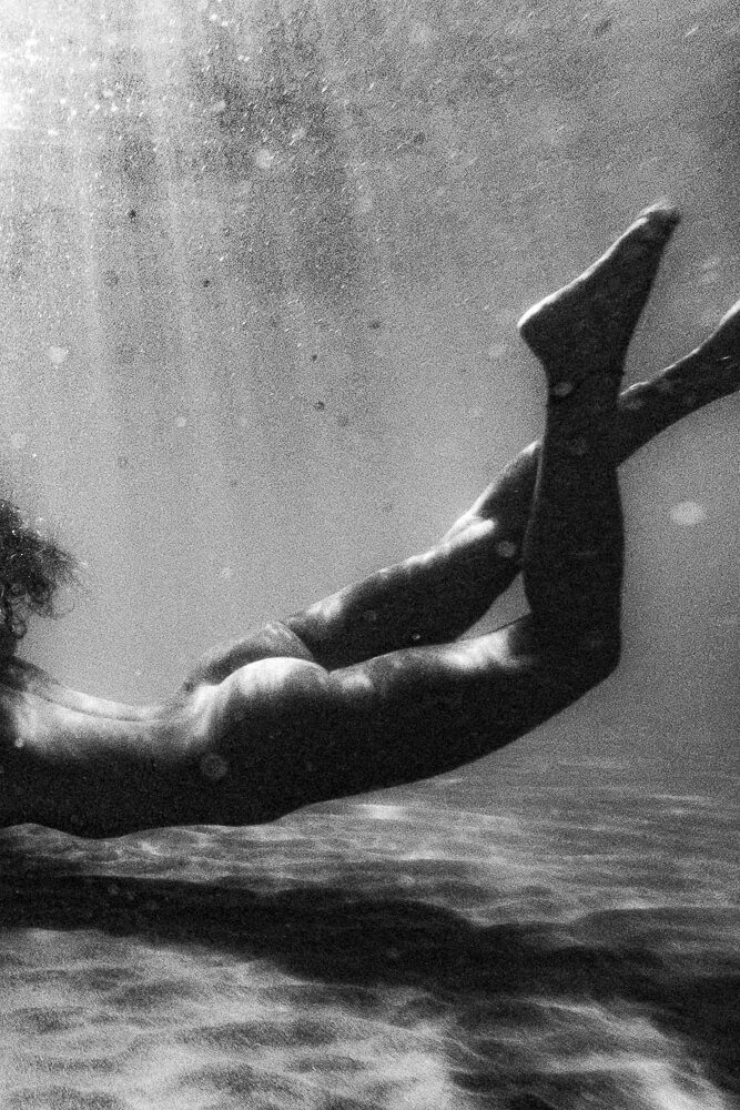 A person swimming underwater, captured from the side, with their body extended and arms reaching forward.