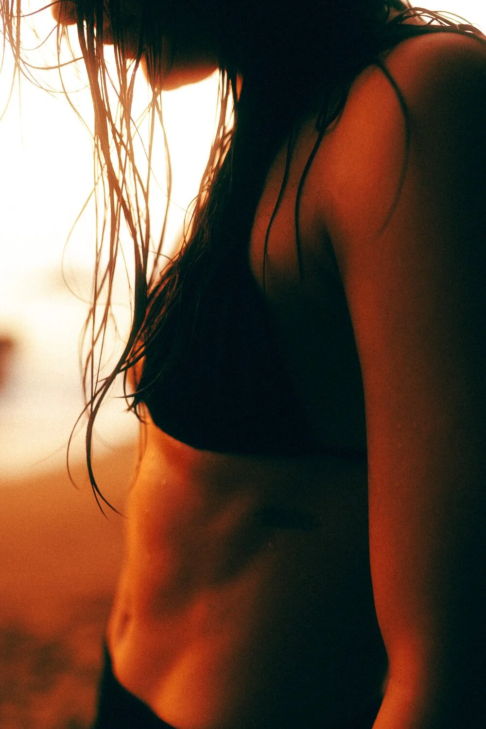 Close-up of a woman with wet hair, wearing a black top, with her midriff exposed, in warm lighting.