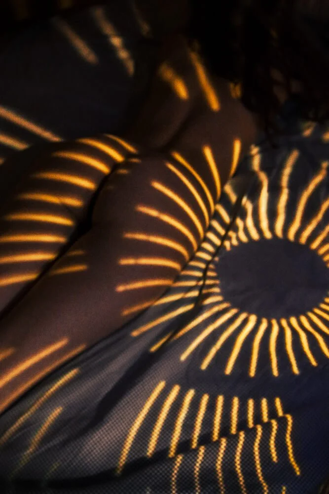 A person laying on a sofa with a pattern of bright, yellowish-orange lines illuminated on their body and the surrounding cushions, creating a radiant, sun-like effect.