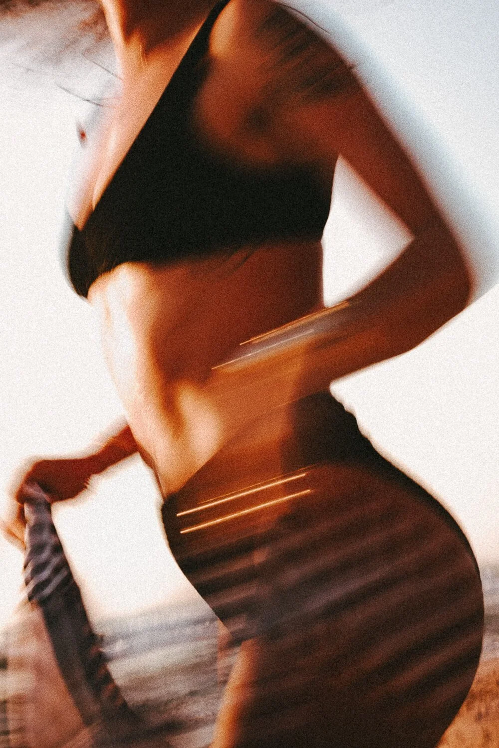 A woman wearing a black sports bra and striped leggings. The photo is taken from the side, capturing her midsection and part of her arm as she runs in an indoor space.