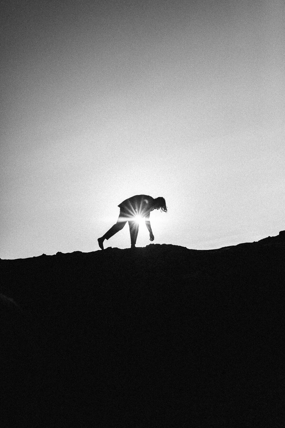 Silhouette of a person climbing an uneven hill at sunset.