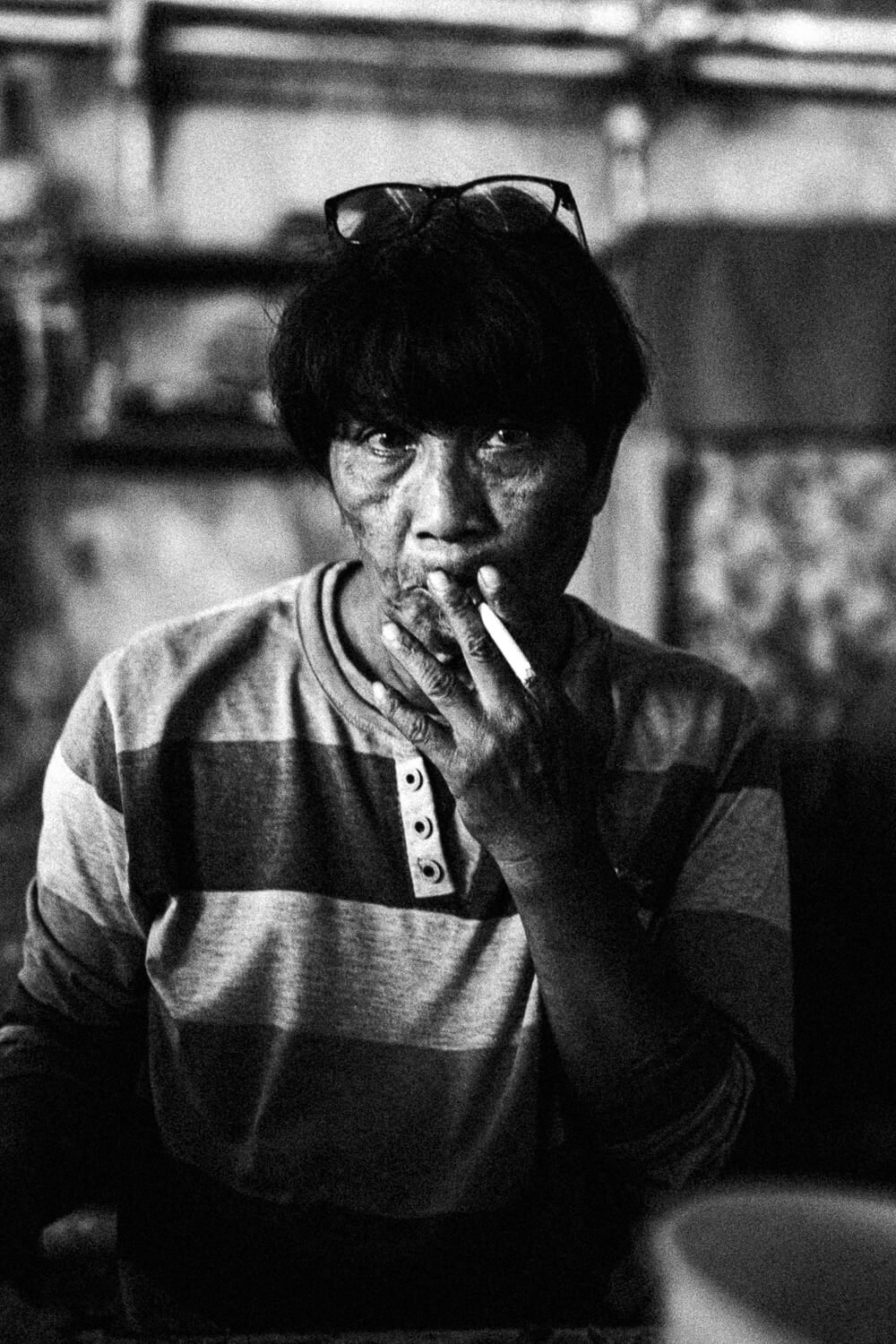 Homme noir avec cheveux noirs, portant un sweat à rayures et des lunettes sur la tête, fumant une cigarette, dans un environnement intérieur