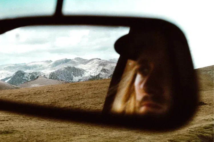 Reflet d'une femme dans le rétroviseur d'une voiture, paysage montagneux en arrière-plan.