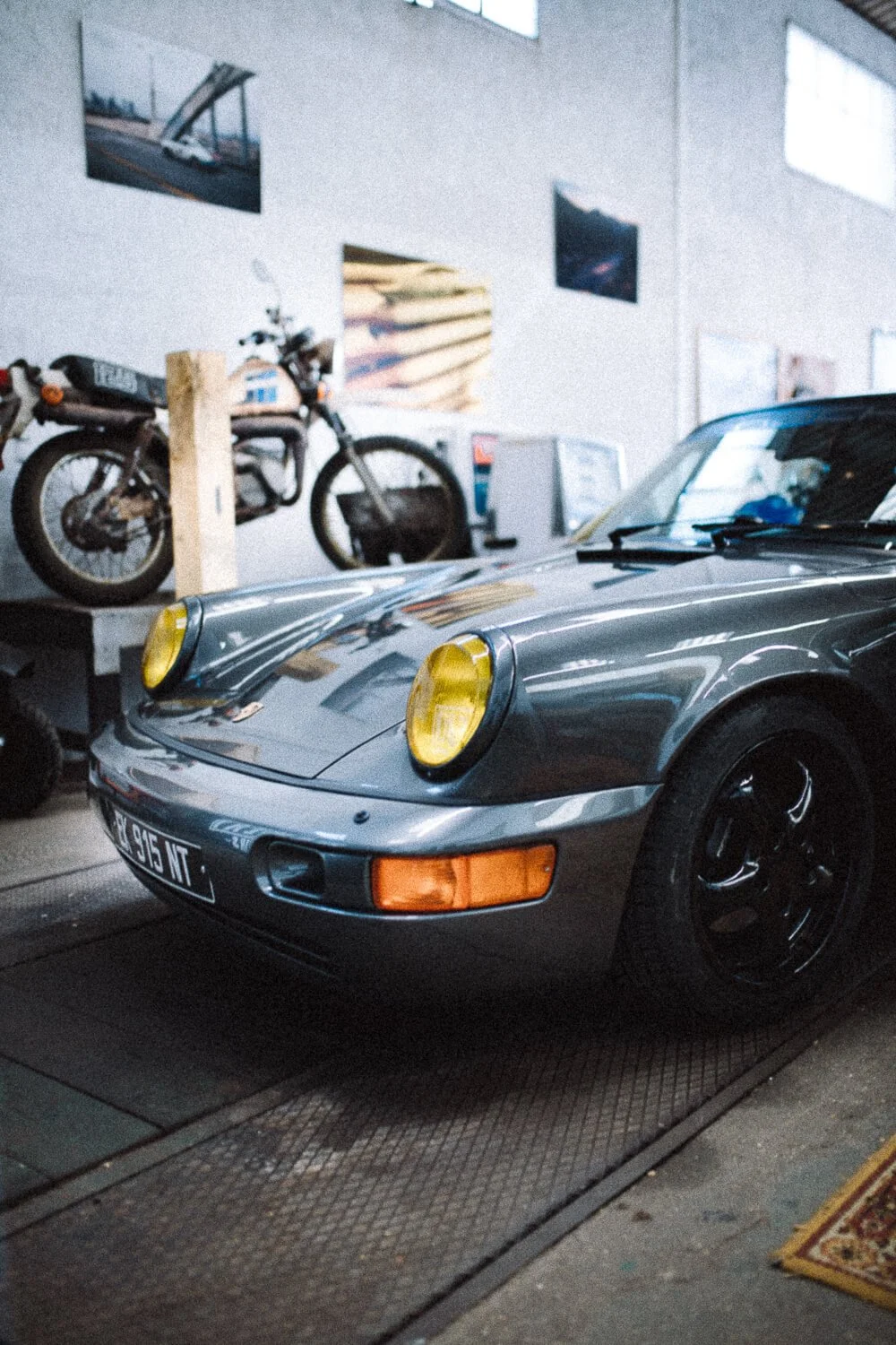 A vintage silver Porsche 911 with yellow headlights parked inside a garage.