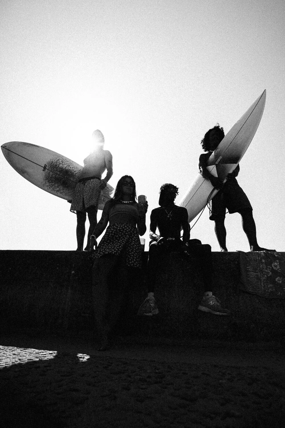 Four people with surfboards at the beach during sunset, silhouetted against the sky.