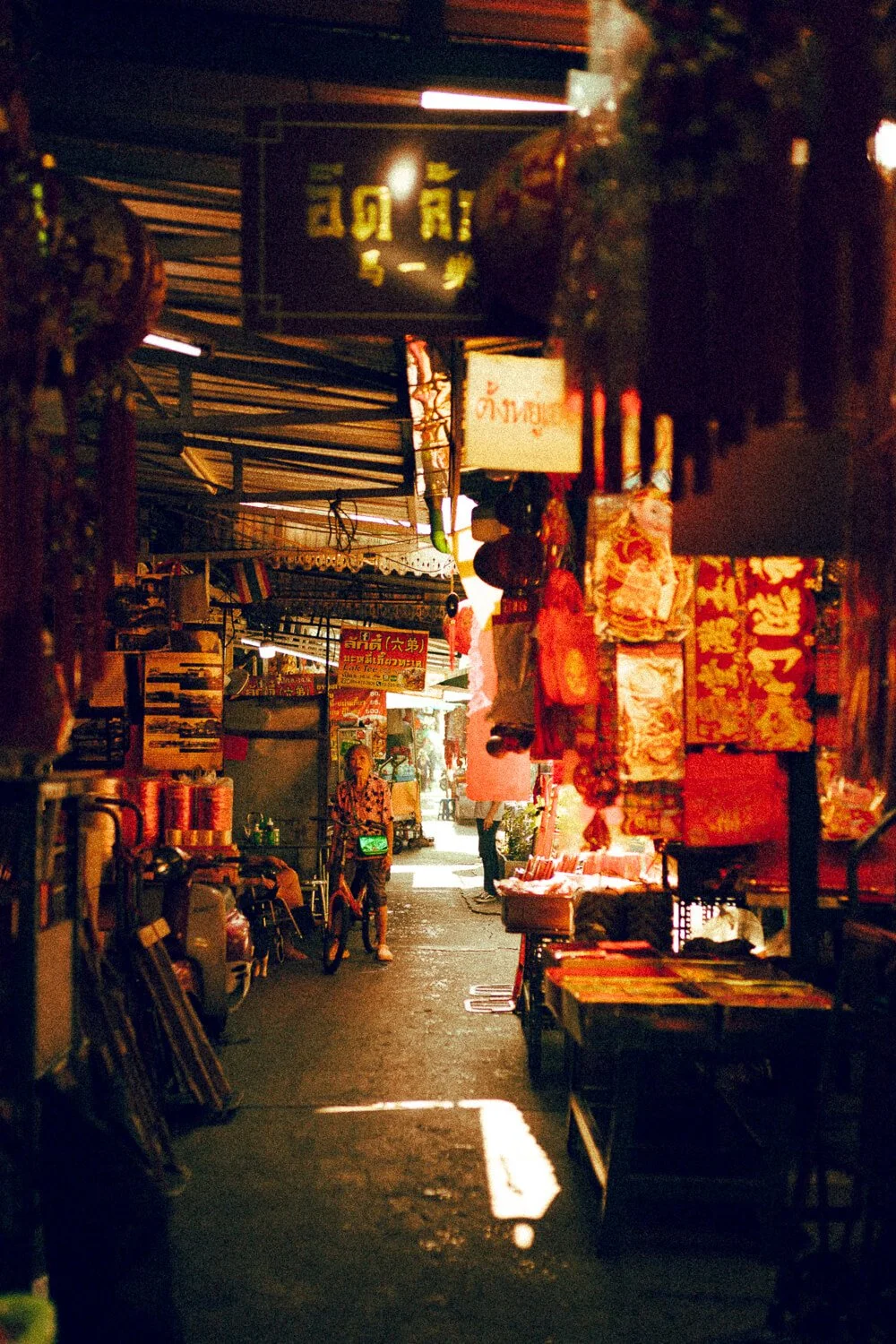 Une ruelle commerçante animée avec des stands de vente de tissus et d'articles traditionnels, à l'intérieur d'un marché nocturne en Asie.