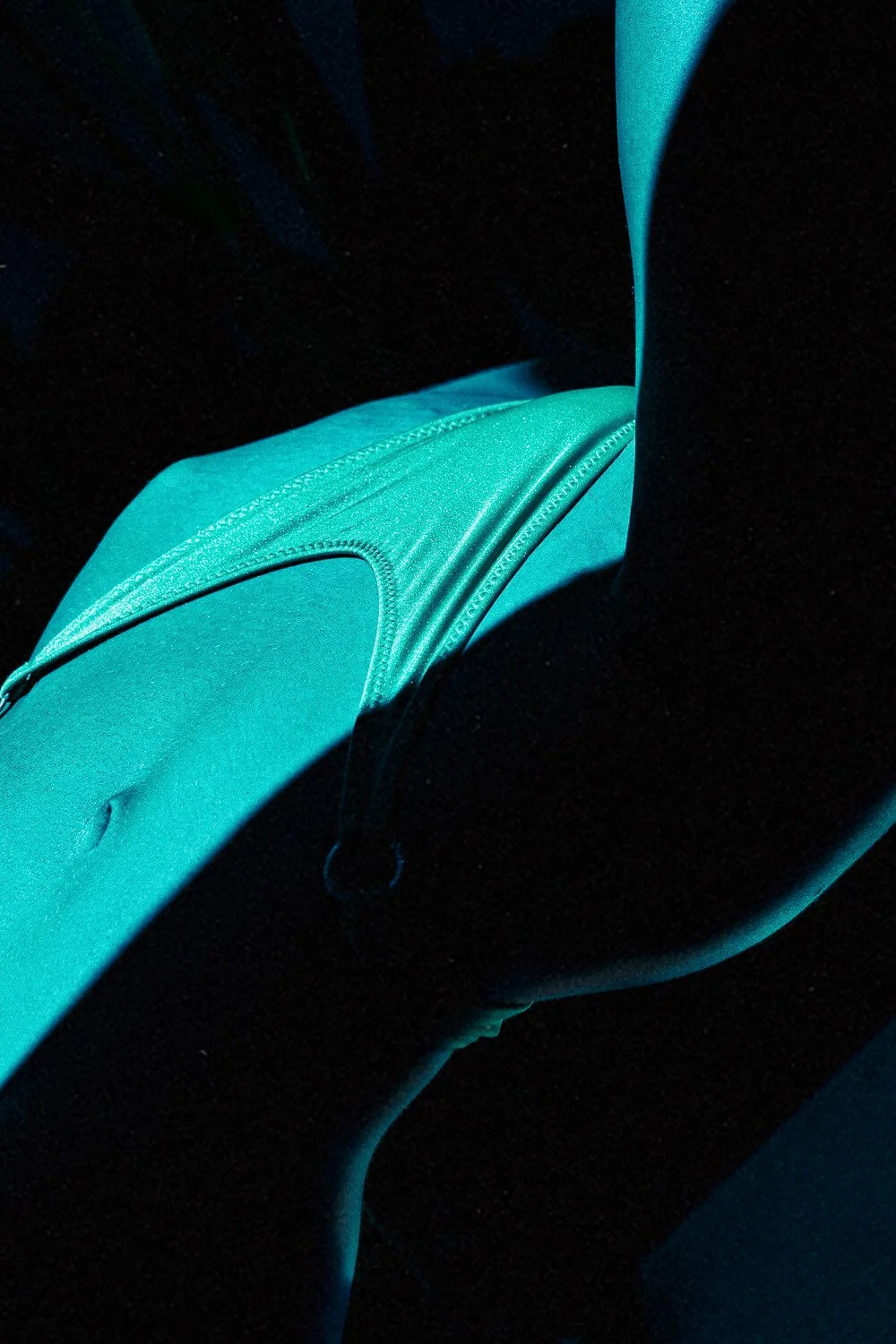 Close-up of a teal-colored backpack on a person's lap, with shadows cast across it.