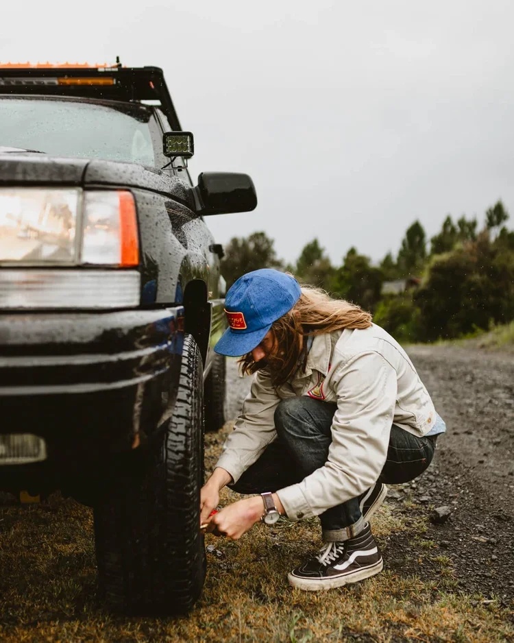 Une femme qui vérifie la pression d'un pneu de voiture sur une route en plein air par temps pluvieux.