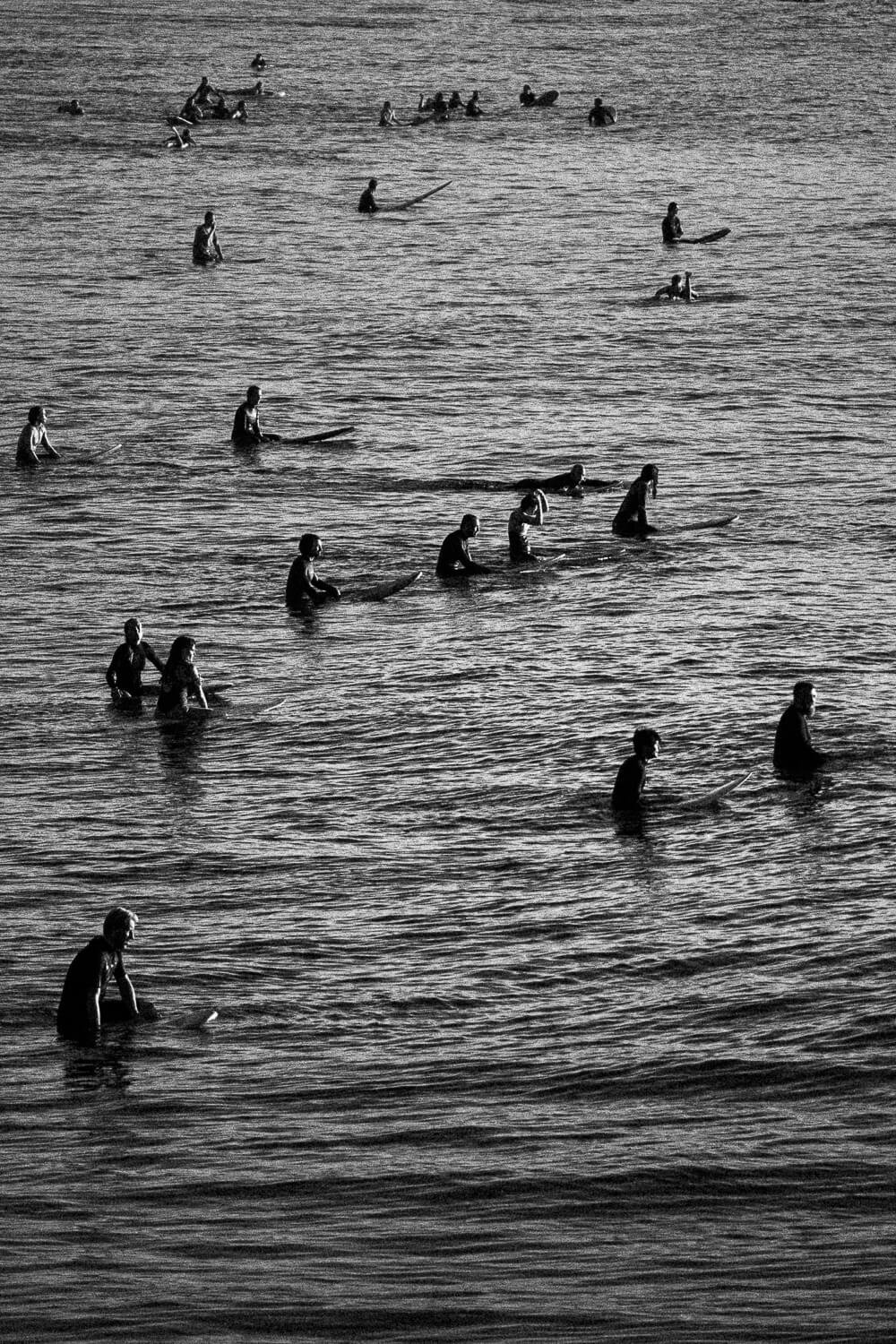 Black and white photo of multiple people in surfboards practicing surfing in the water.