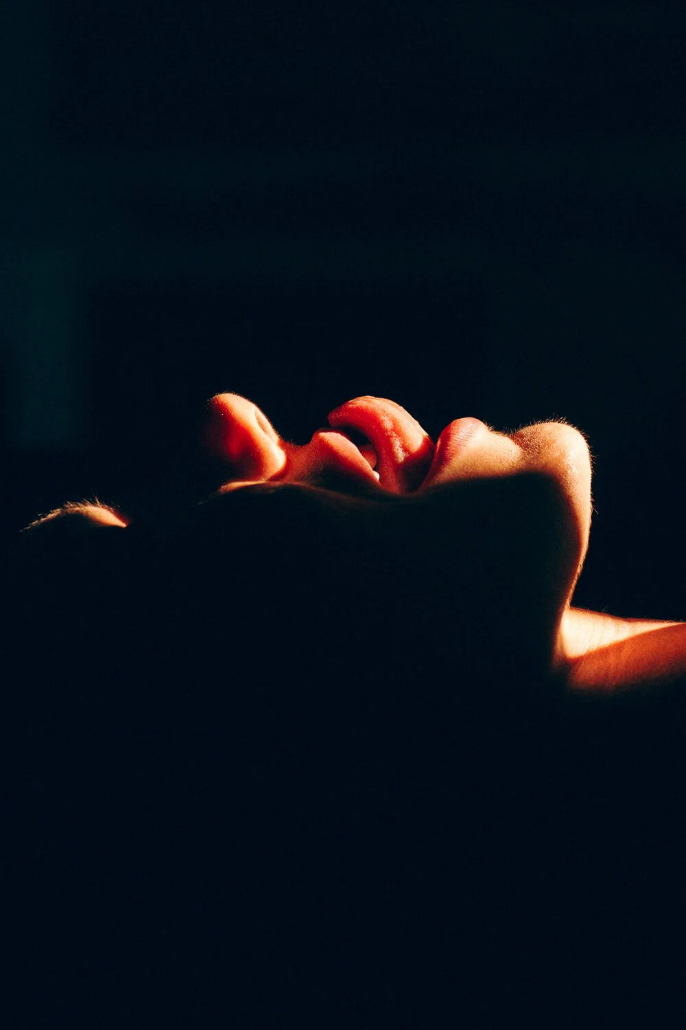 A hand with fingers curled, illuminated by a warm light, set against a dark background.