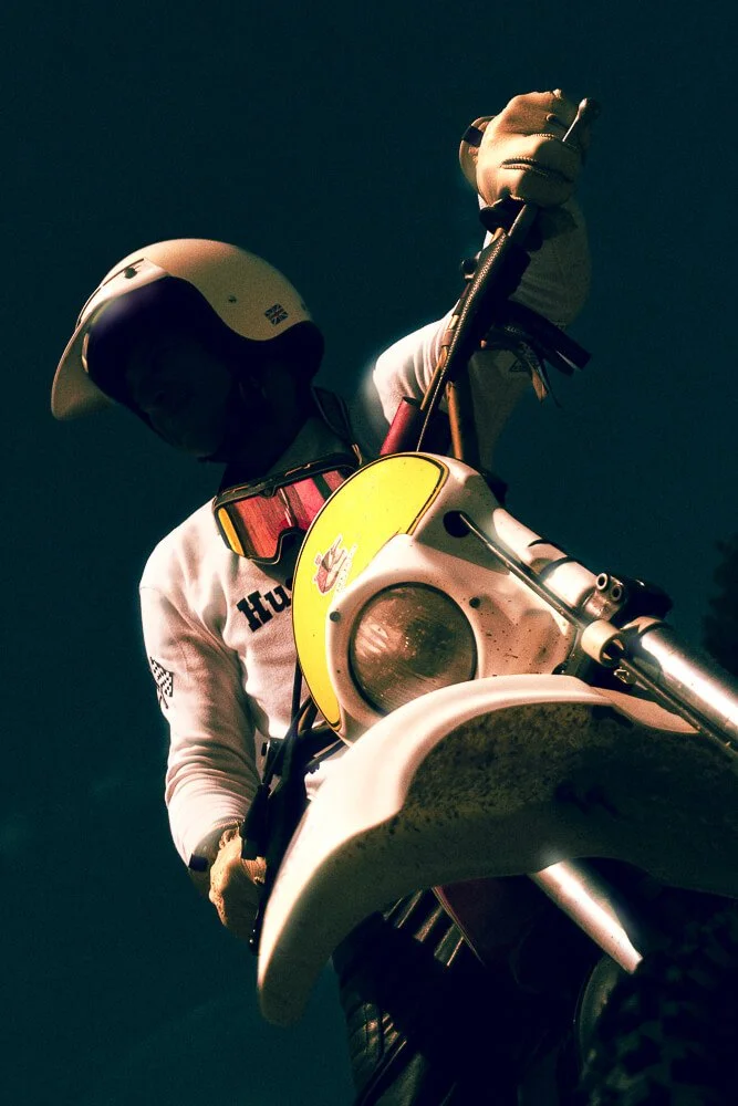 A person wearing a helmet and gloves riding a dirt bike upward against a dark sky.