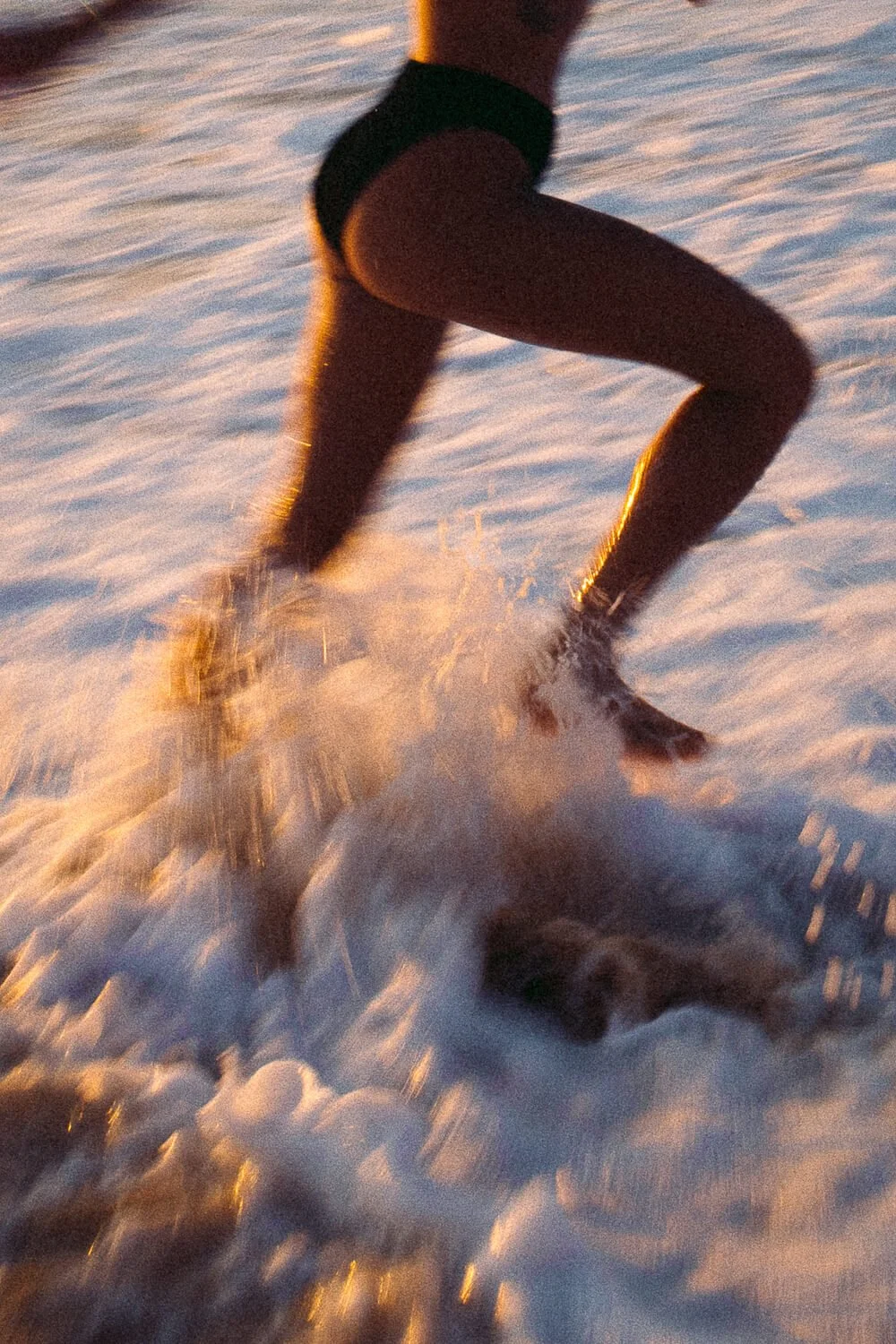 Person running on wet sand or beach at sunrise or sunset, with water splashing around their feet.