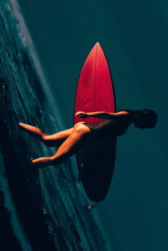 A woman in a wetsuit leaning on a surfboard on the water at night.