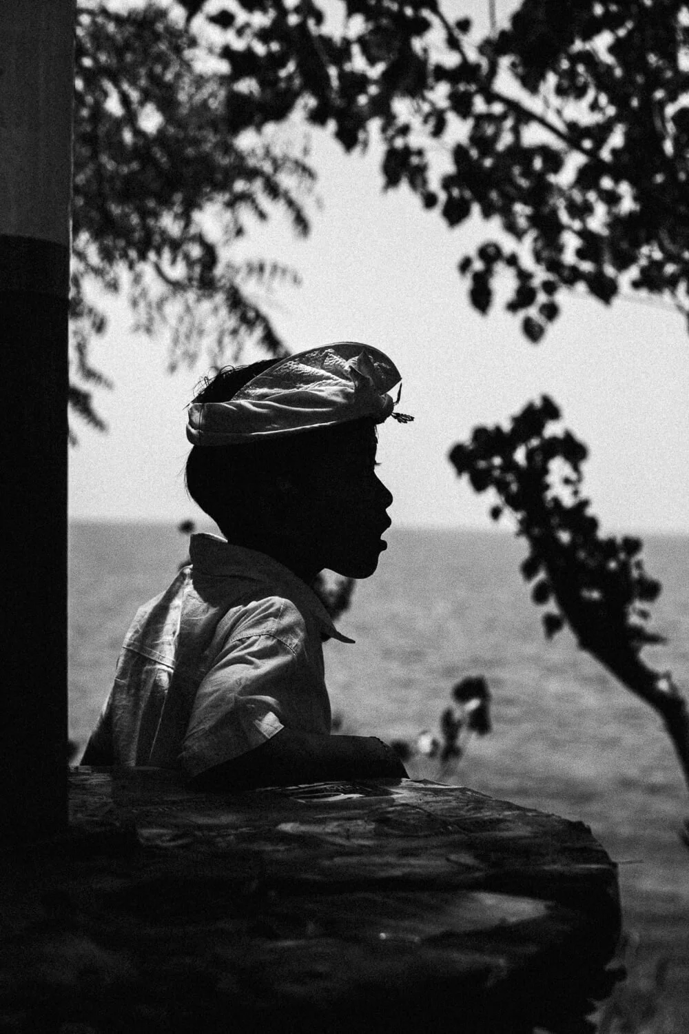 Silhouette d'un garçon regardant la mer, avec arbres en arrière-plan, en noir et blanc.