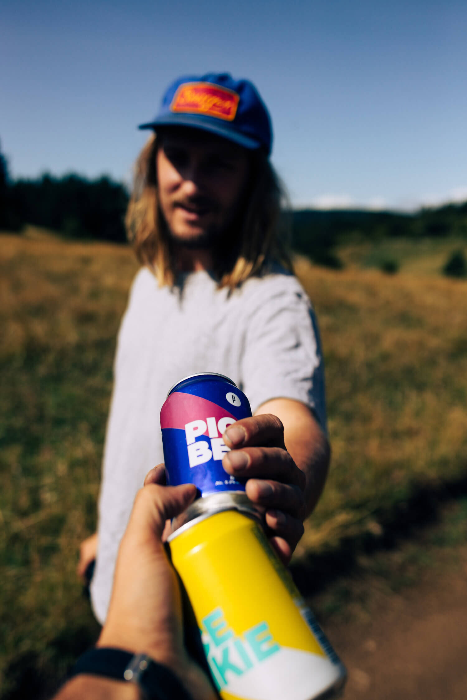 Personne tendant une canette de boisson bleue à une autre personne, extérieur.