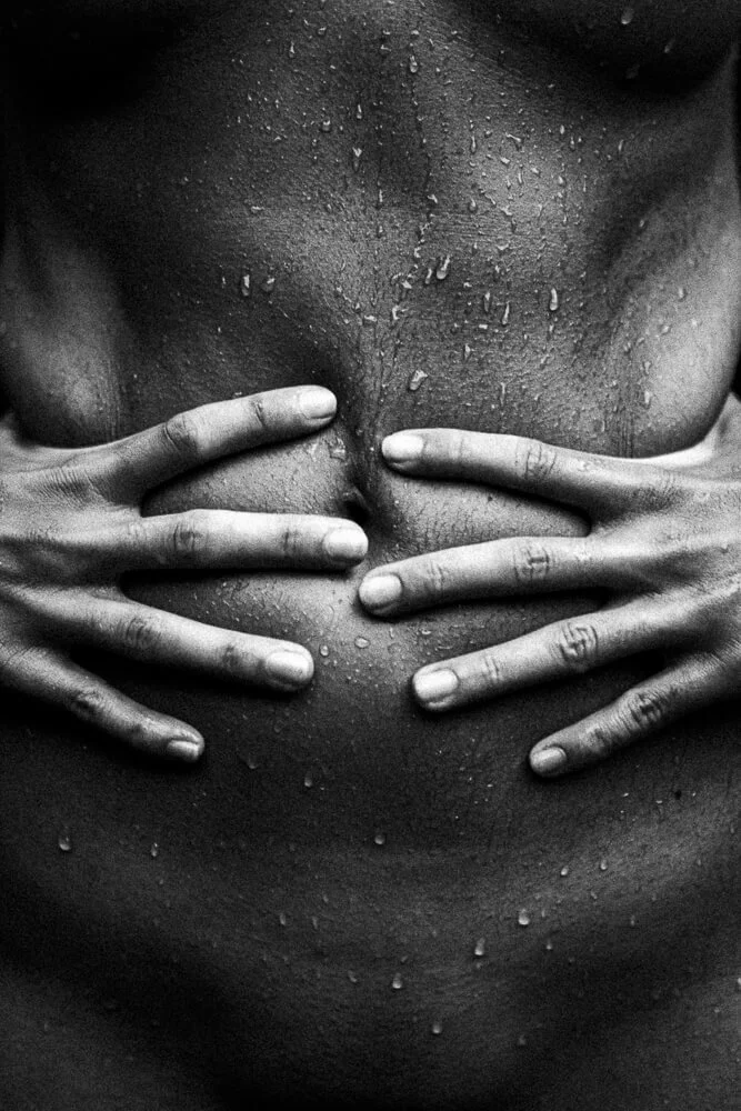Close-up of a person's wet, bare chest being gently squeezed by their hands.