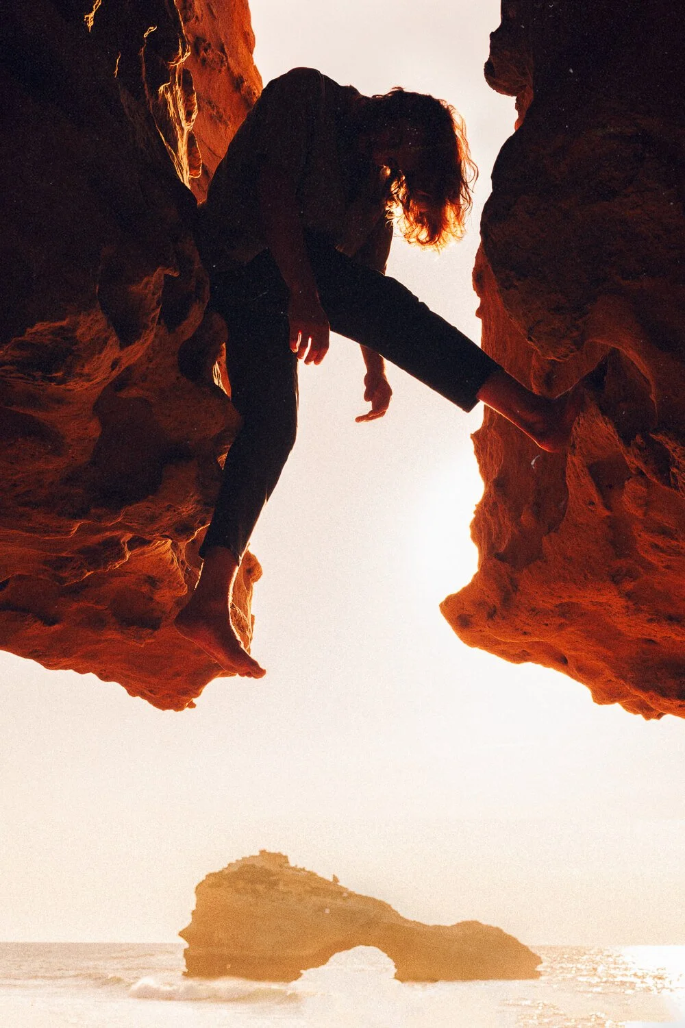 Person bouldering at sunset on a rocky cliff near the ocean.