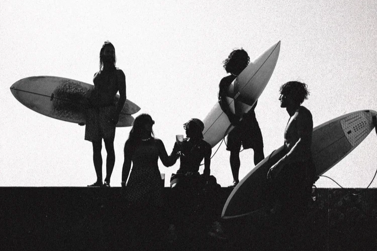 Groupe de personnes avec des planches de surf, discutant et passant un moment ensemble sur la plage au coucher du soleil.
