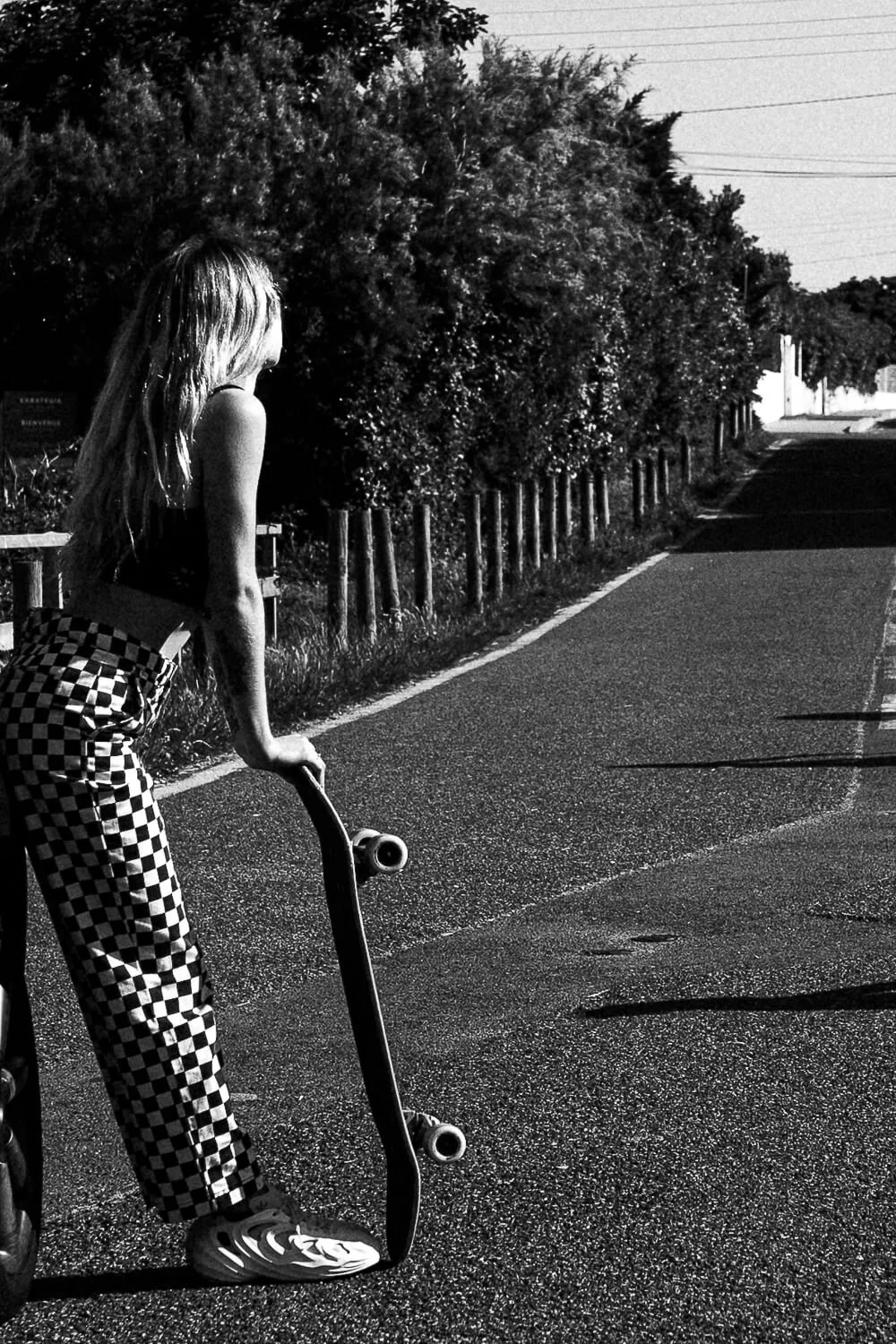 Young woman with long hair holding a skateboard on a quiet road, black and white photo.