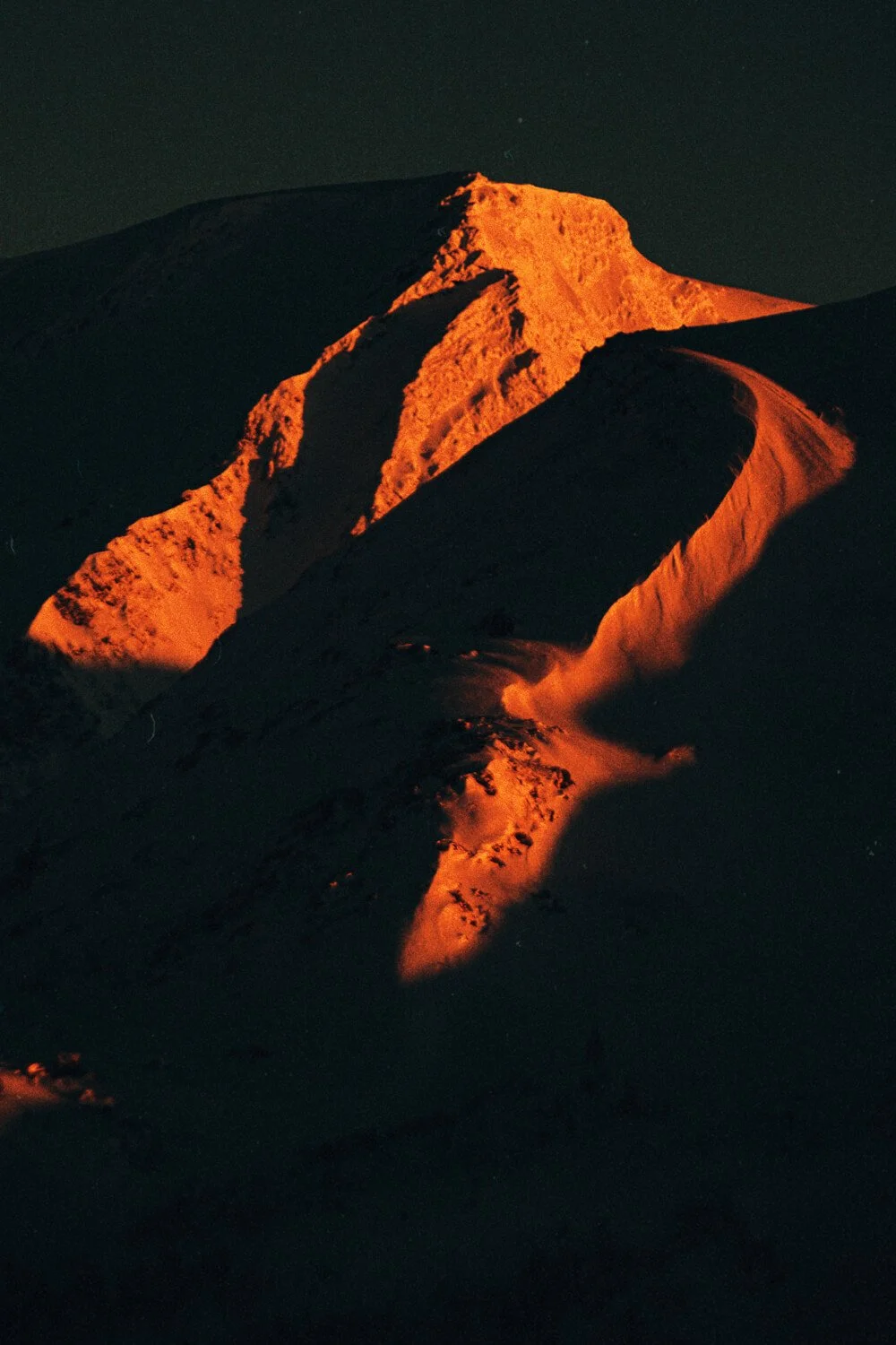 Photo d'une montagne enneigée éclairée par la lumière du coucher de soleil, dans un ciel nocturne.