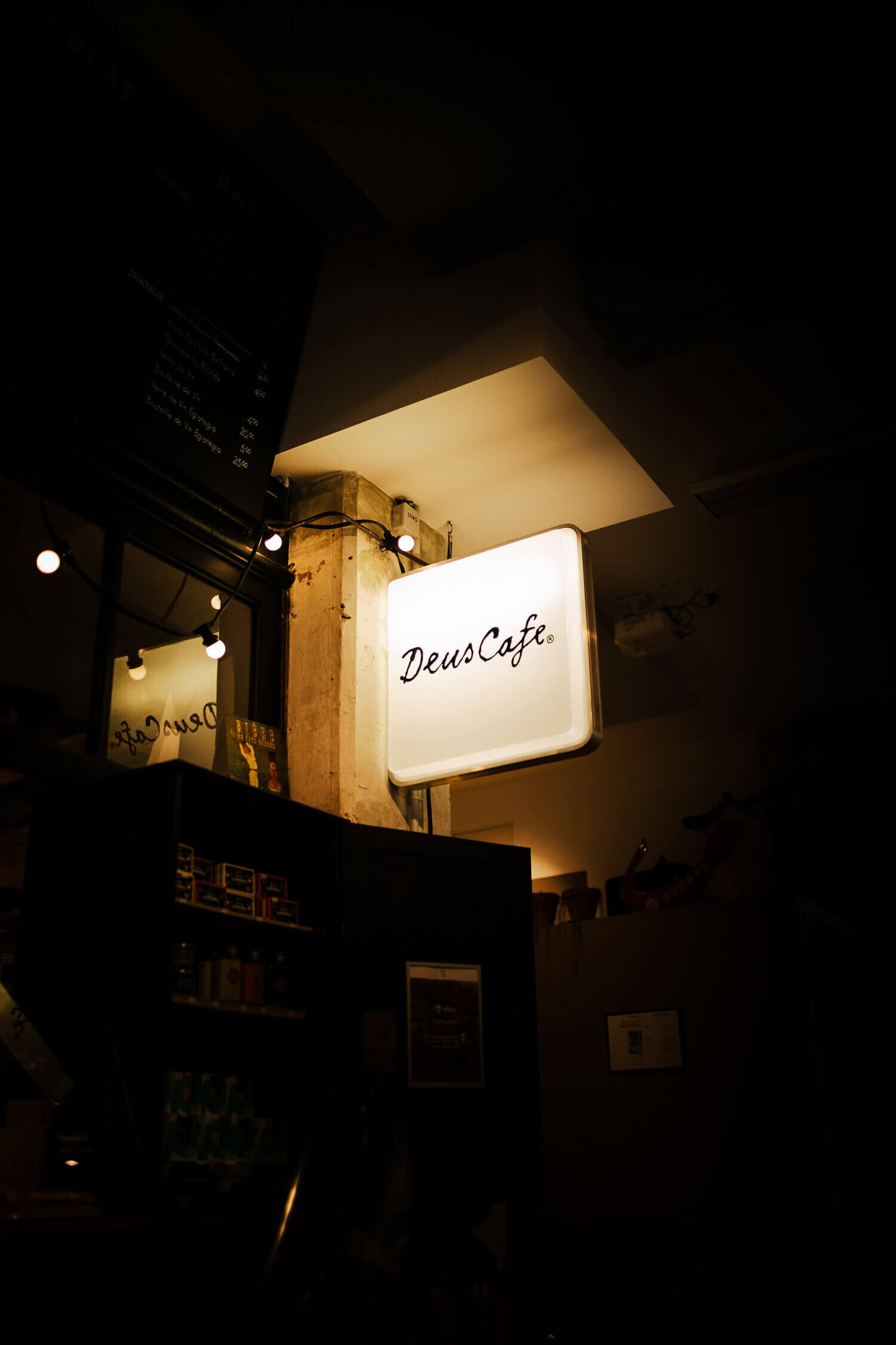 Enseigne lumineuse indiquant « Deus Café » à l'intérieur d'un café, avec ambiance tamisée et éclairage doux.