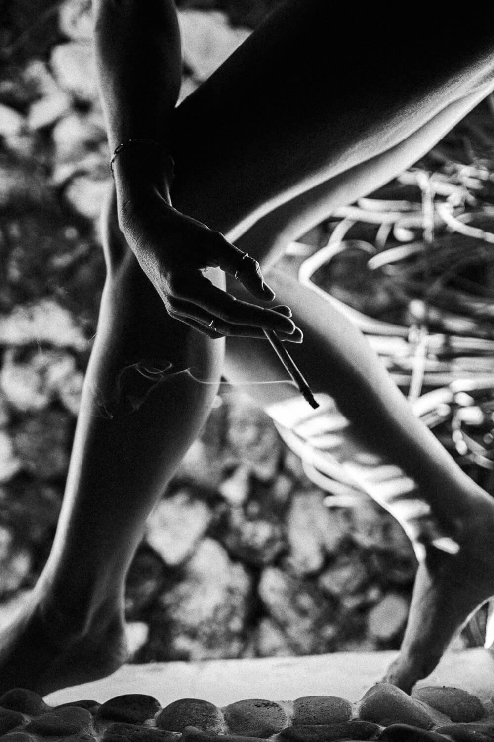 A person drawing or writing on a skeleton or life-sized human figure while seated outdoors, with rocks and foliage in the background.