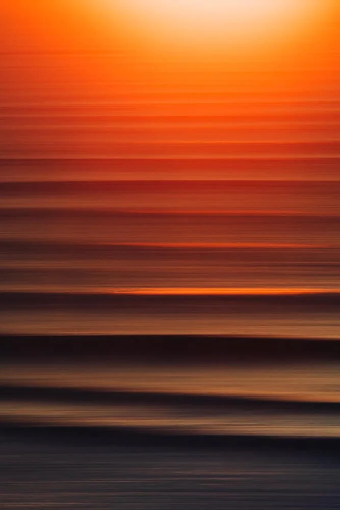 Blurred image of a sunset over water with orange and dark tones.