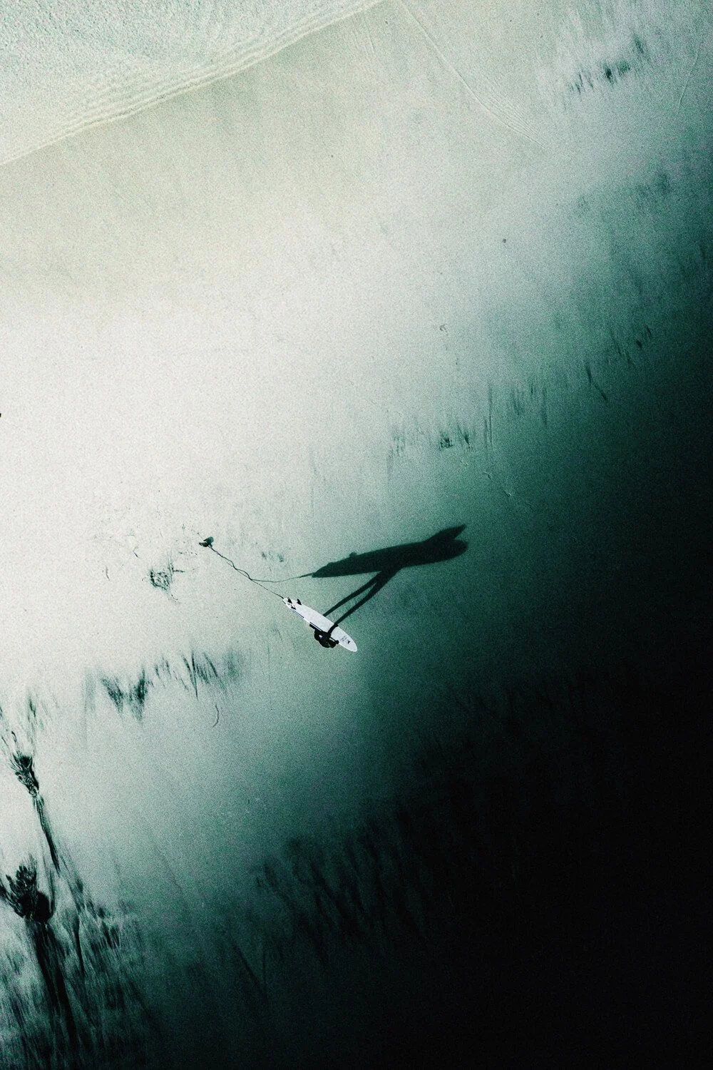 Une personne fait du paddle dans un lac ou une mer calme avec une longue ombre projetée sur l'eau, la photo prise d'en haut.