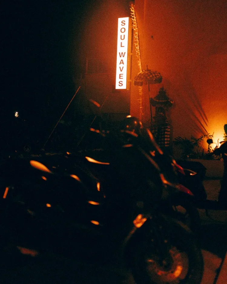 Une enseigne au néon rouge indique 'Soul Waves' dans une atmosphère sombre et brumeuse, avec des motos en premier plan et une structure architecturale derrière.