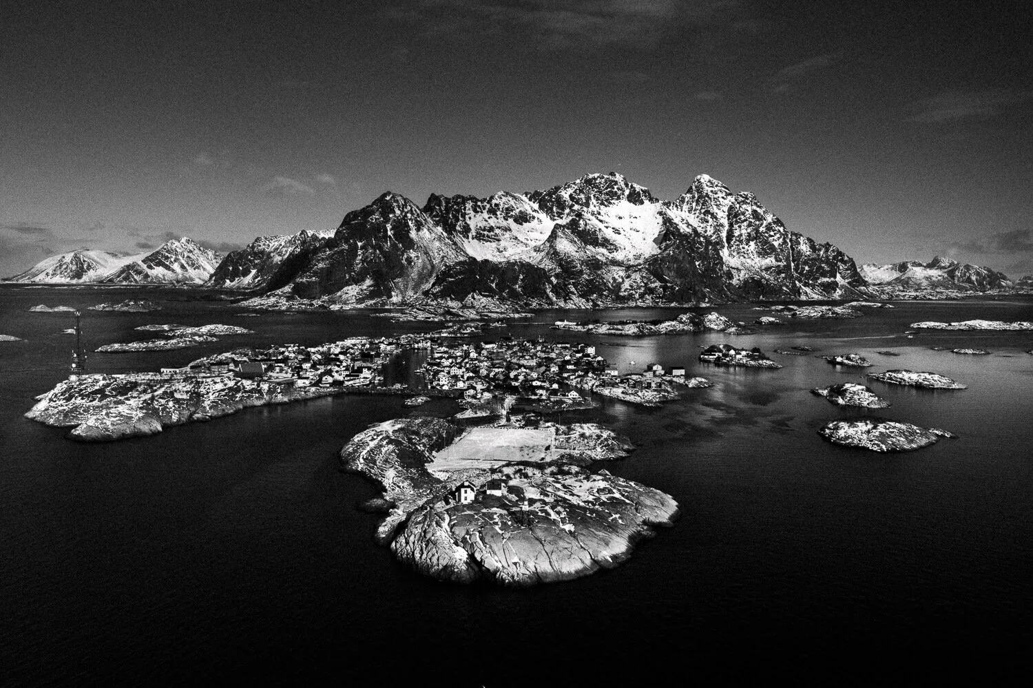Vue aérienne d'un paysage arctique avec plusieurs îles et une montagne enneigée en arrière-plan, en noir et blanc.