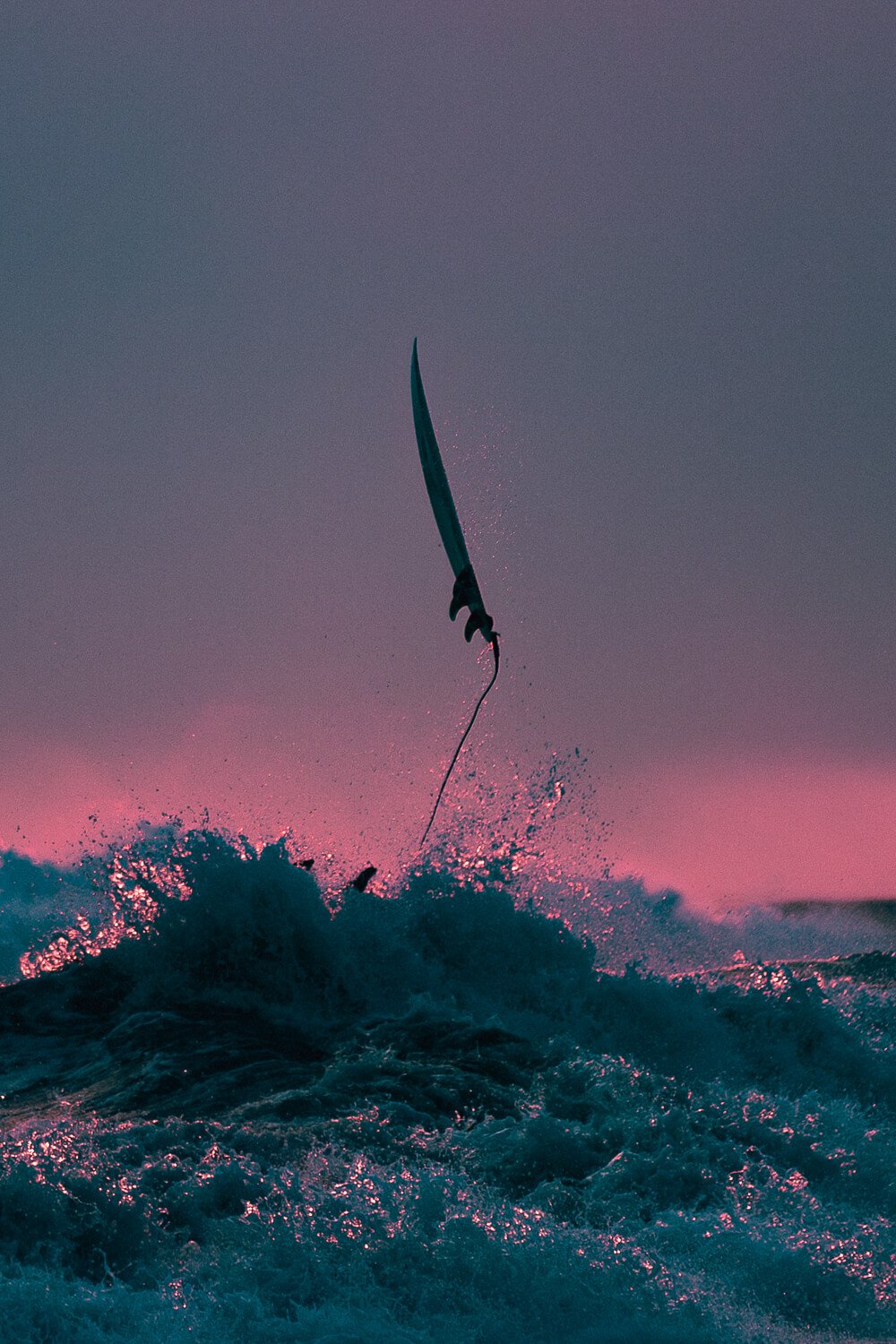 Un kiteur de kite surf en plein saut à la tombée de la nuit, avec le ciel coloré en rose et violet.