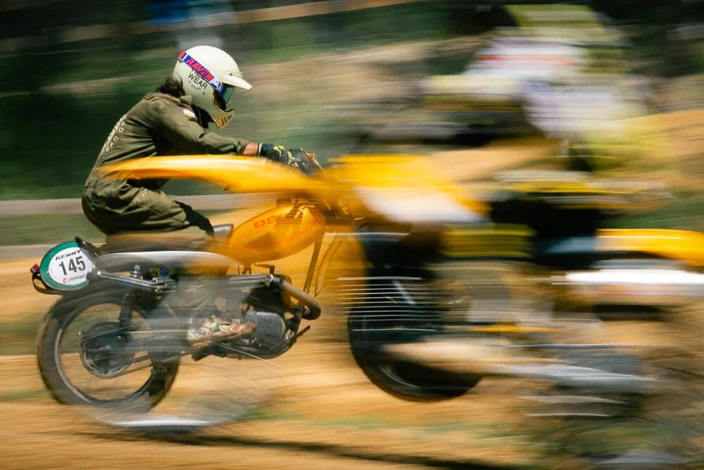 A motorcycle racer in a helmet and racing gear is speeding on a yellow motorcycle on a dirt track, with a blurred background indicating high speed.
