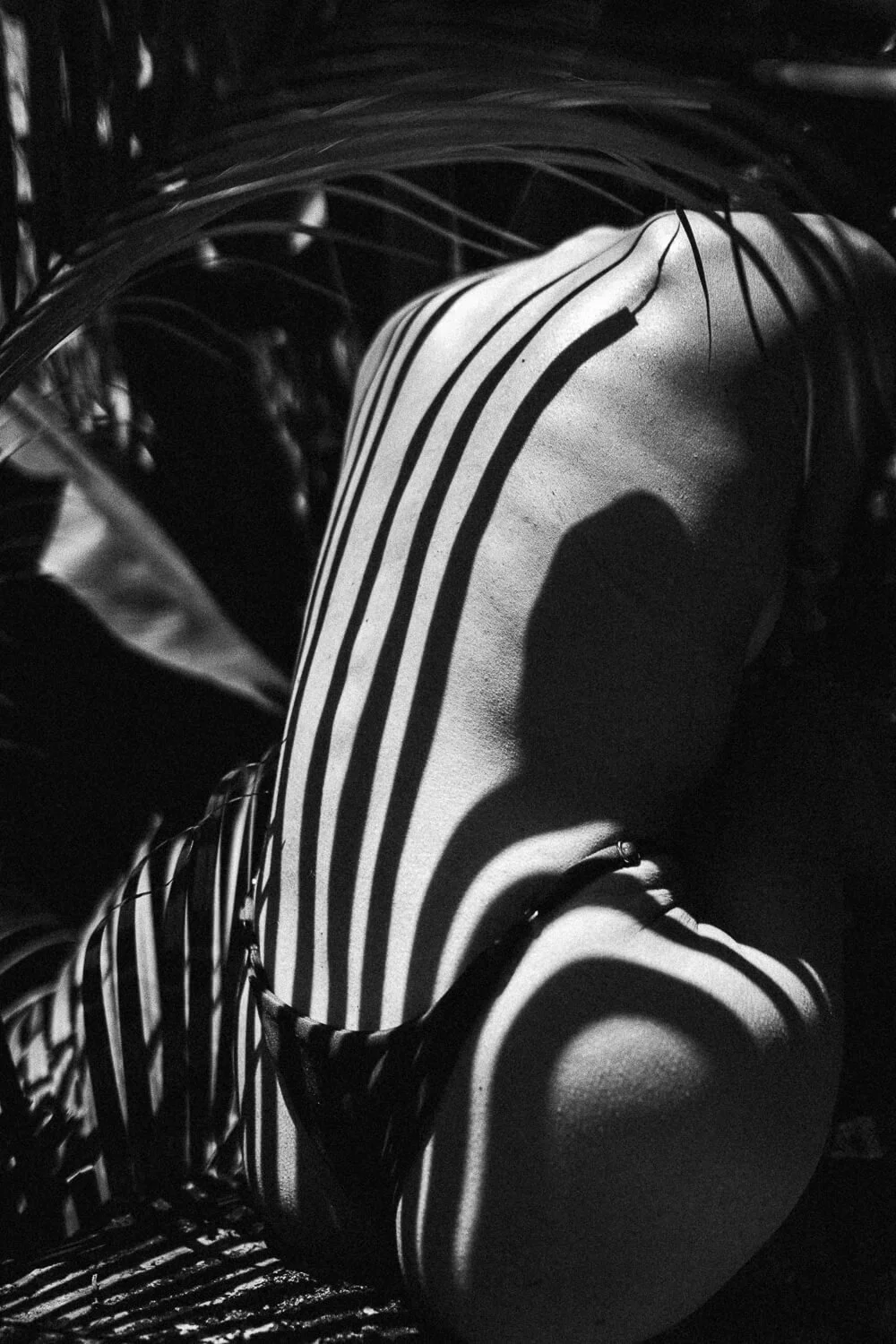 Close-up of a face sculpture with shadows cast by nearby window bars, creating striped patterns in black and white.