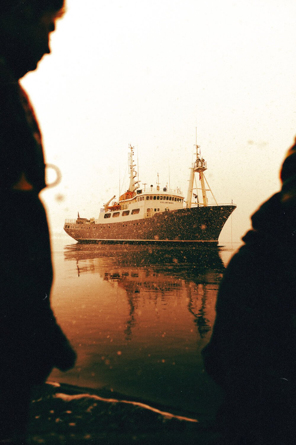 Deux personnes en silhouette regardant un bateau au loin sur l'eau lors d'un coucher de soleil.