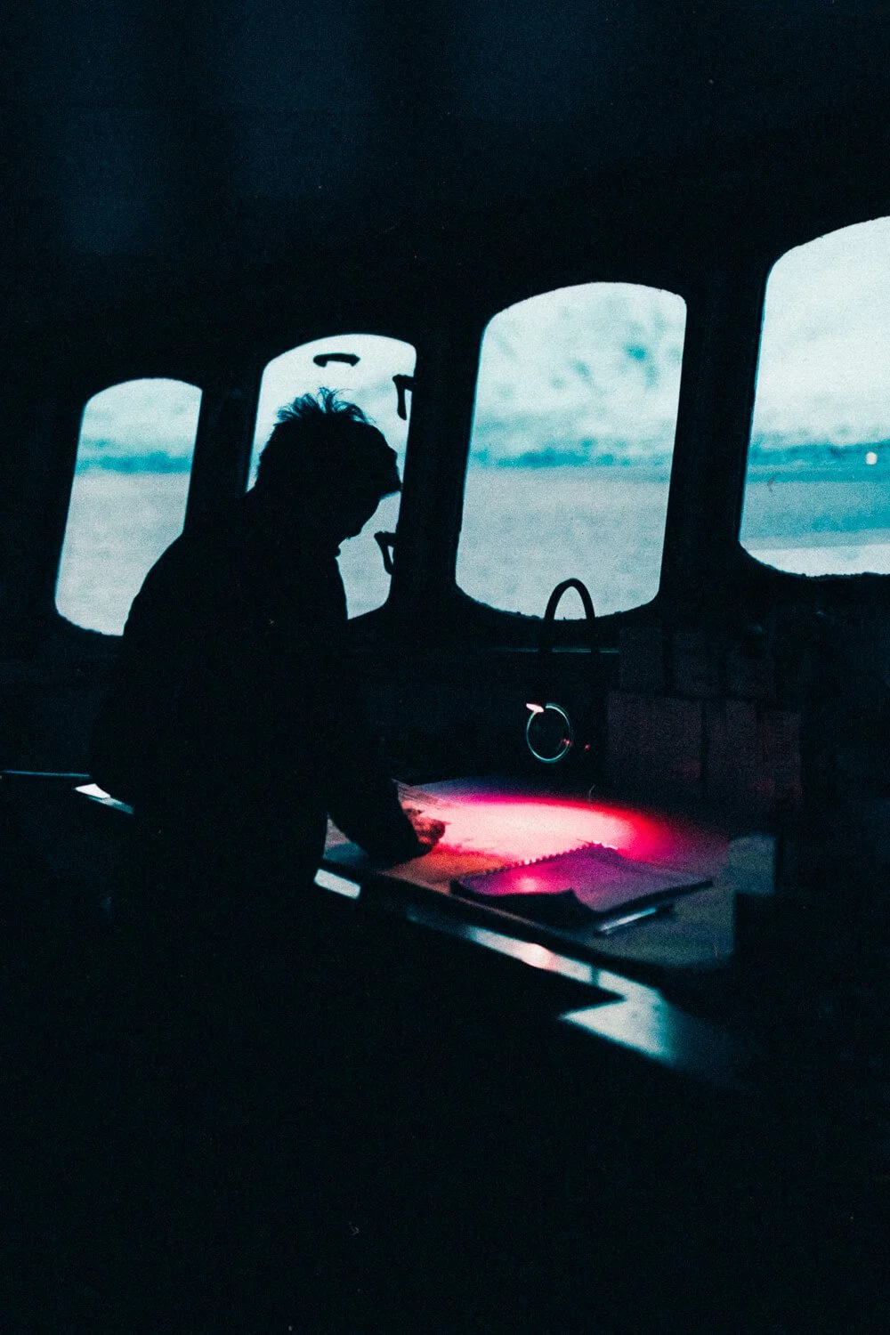 Silhouette d'une personne à l'intérieur d'un avion, regardant un livre ou un carnet, avec vue sur l'extérieur par les fenêtres.