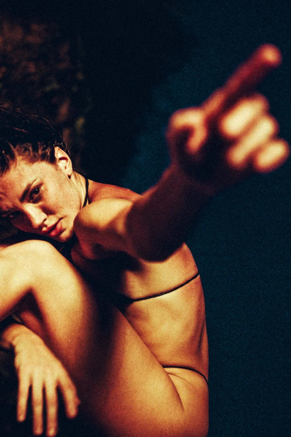 A woman with braided hair and a serious expression extending her hand toward the camera in a dark setting.