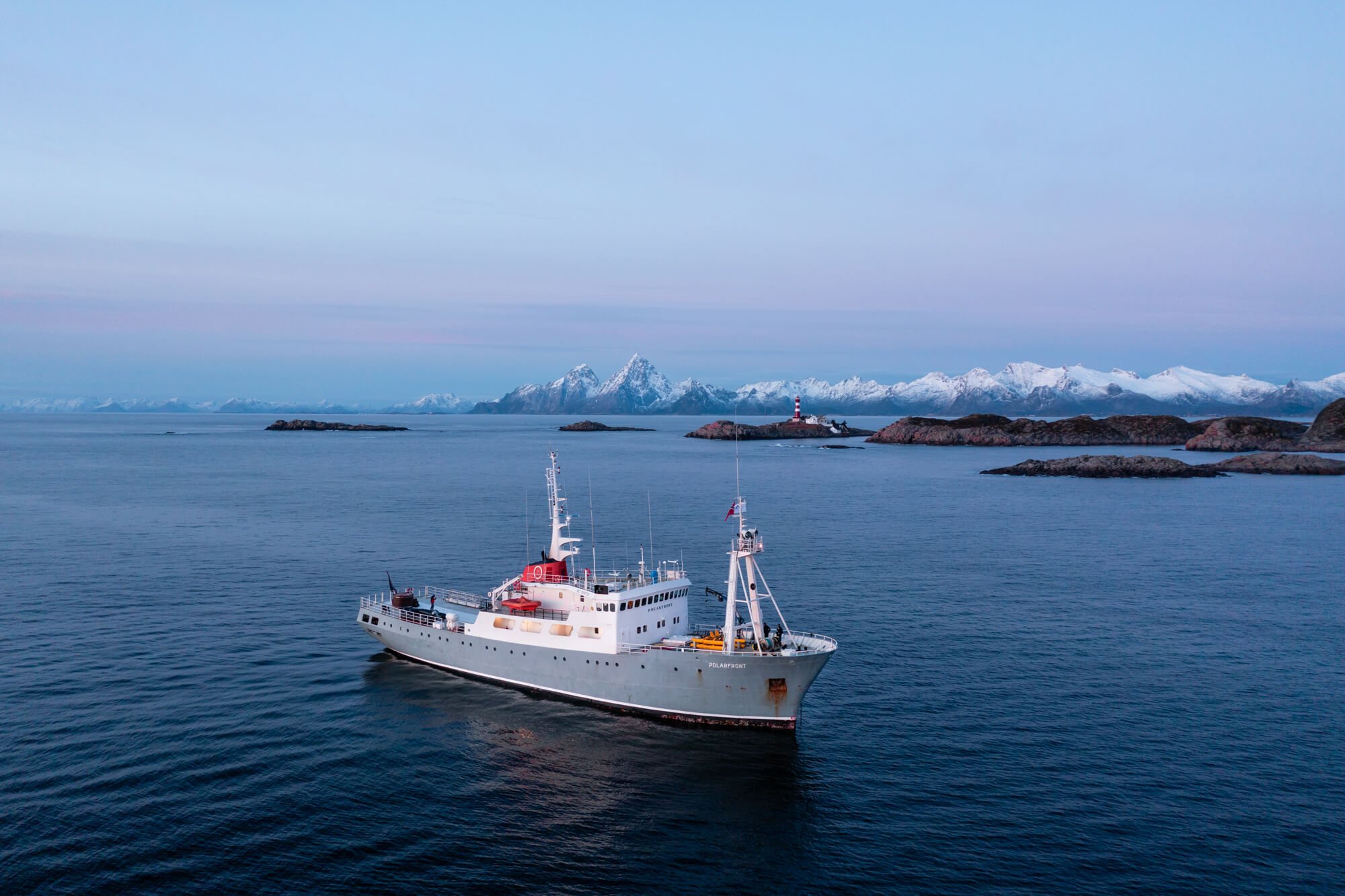 Navire blanc en mer avec un paysage de montagnes enneigées et un phare en arrière-plan.