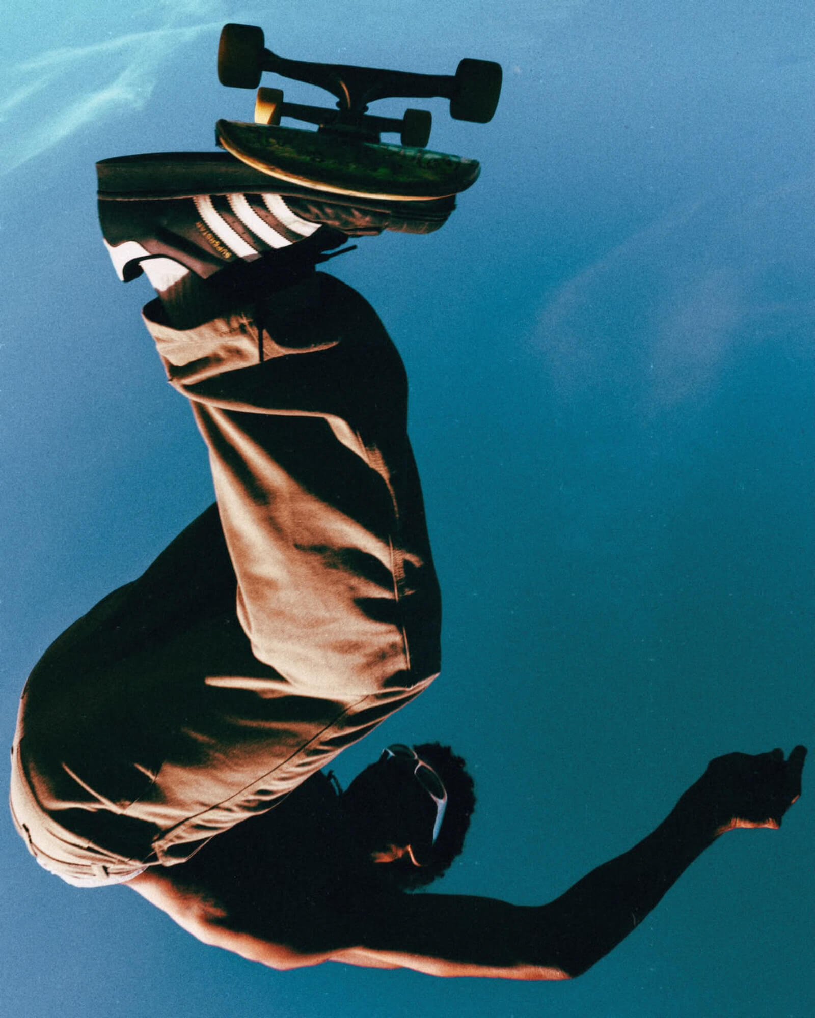 A person wearing a striped t-shirt and beige jacket. The person is on a skateboard with black wheels, riding on a smooth surface during the evening or night, with a dark sky in the background.