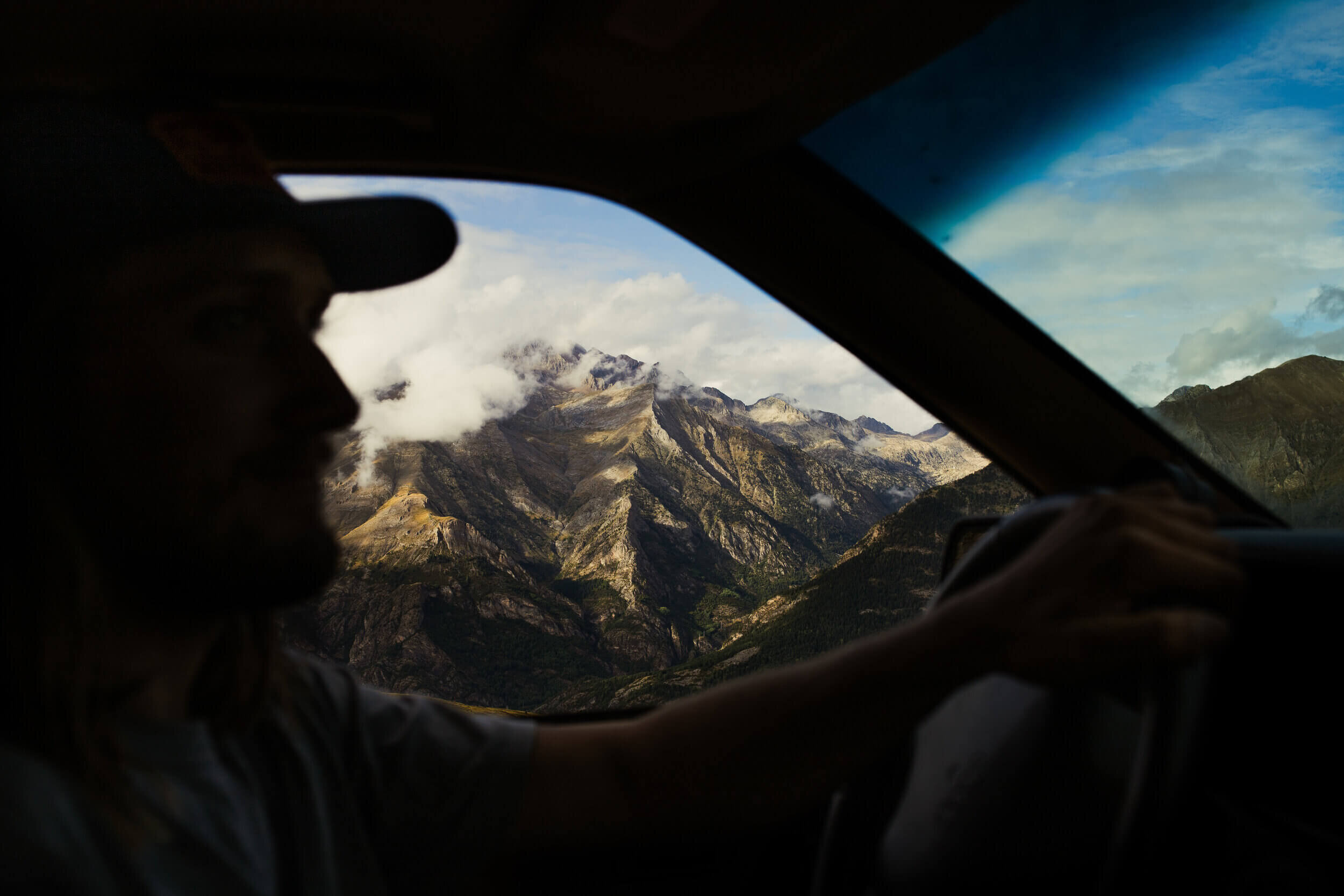 Vue des montagnes à travers la fenêtre d'une voiture avec une personne au volant.