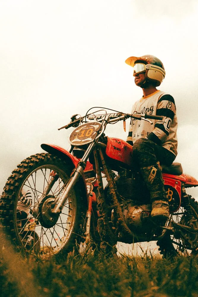 A person wearing a helmet and goggles sitting on a dirt bike on a grassy field.